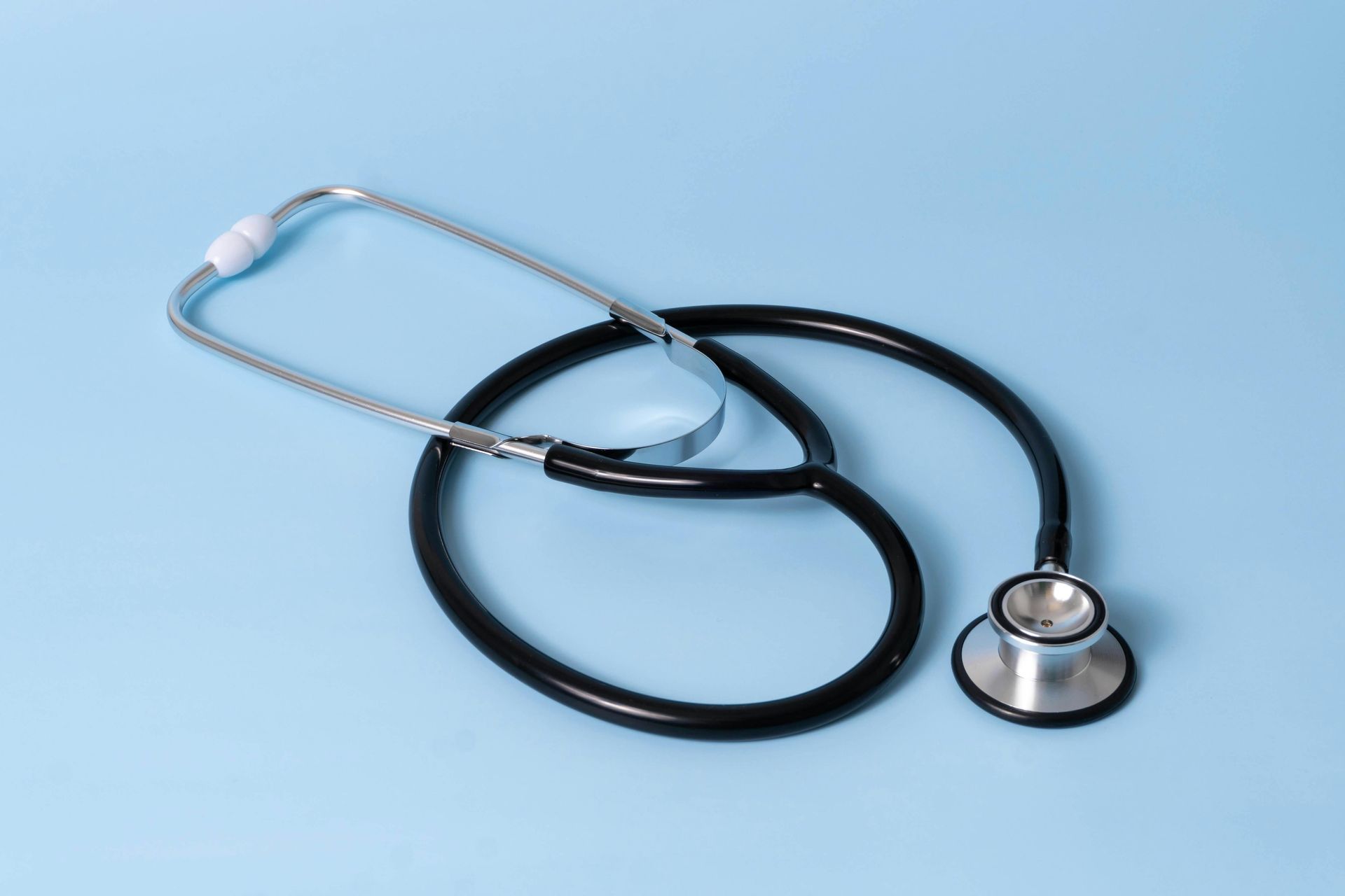 Black stethoscope on a light blue surface.