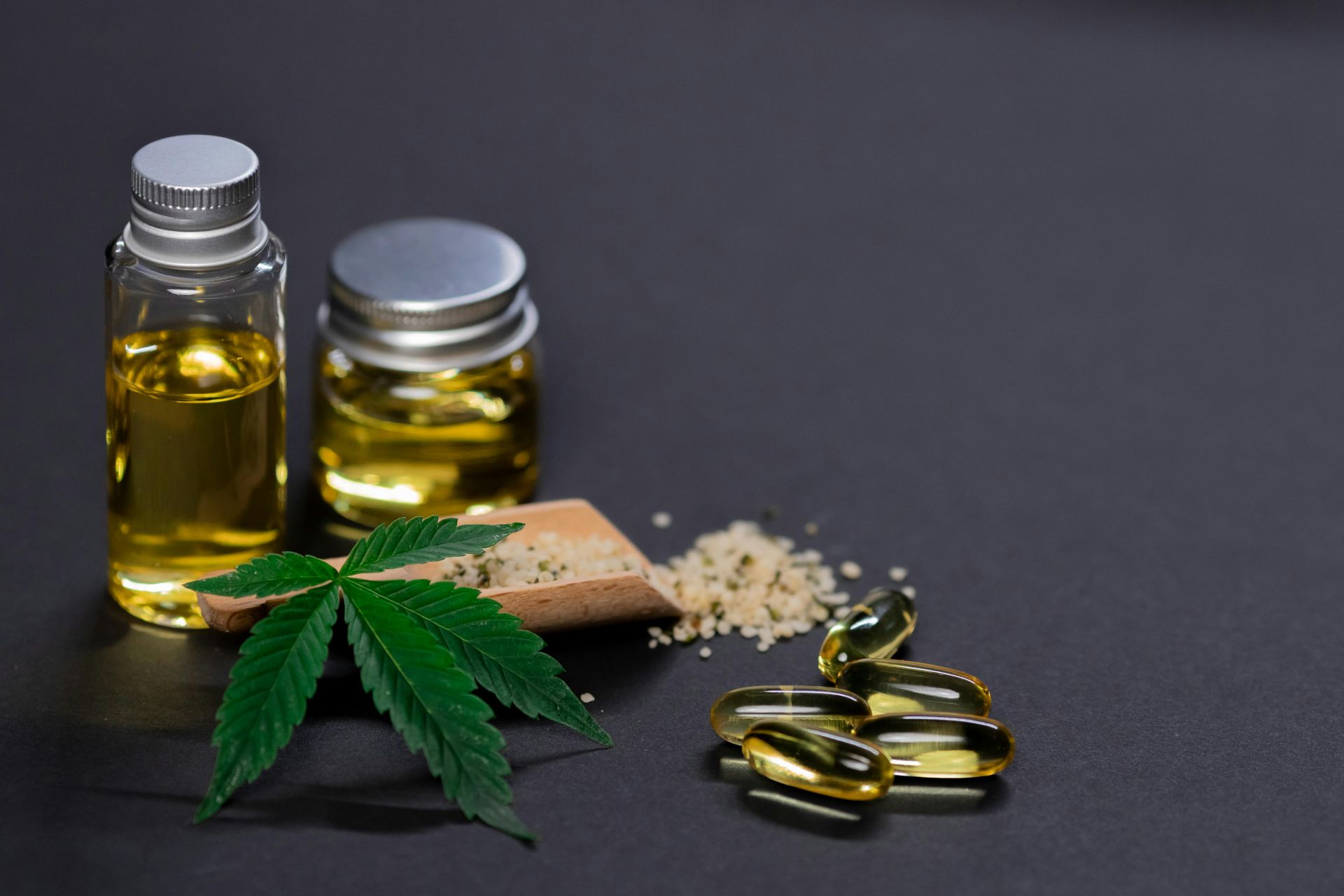 CBD products: bottles of oil, capsules, hemp leaf, and seeds on a dark background.