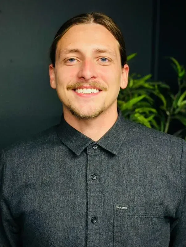 Man with long hair pulled back, smiling, wearing a dark gray button-down shirt.