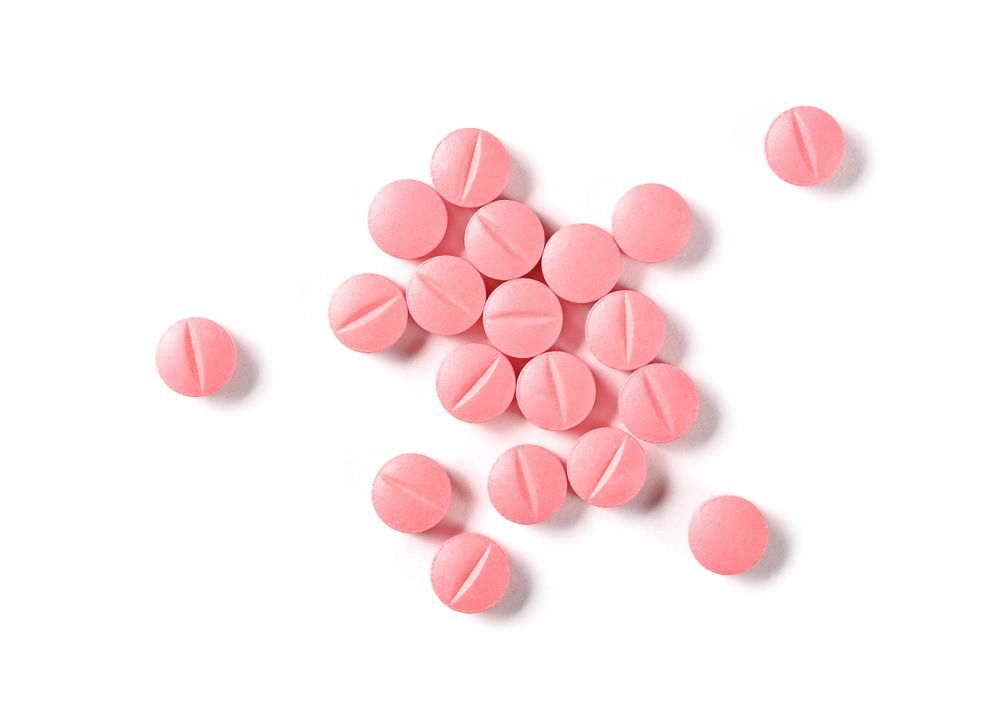 Pink, round pills scattered on a white surface, each with a scored line.