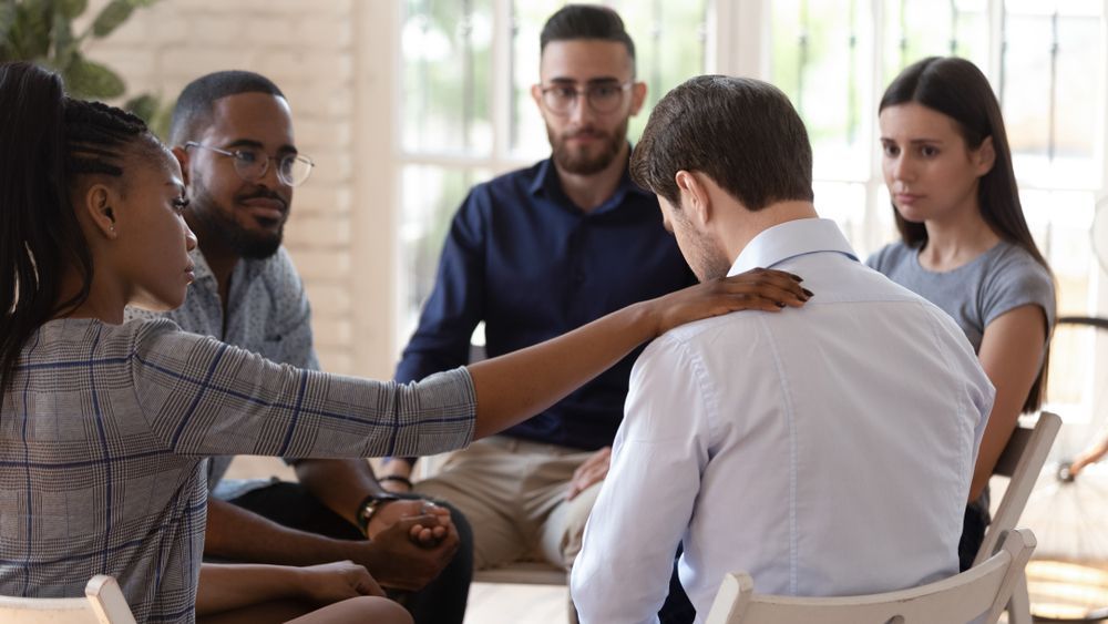 Group therapy session: a person is comforted by another, while others look on in support.