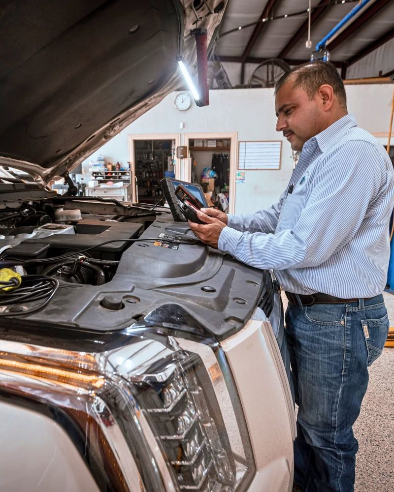 Mechanic inspecting a tablet beside an open car hood in a garage