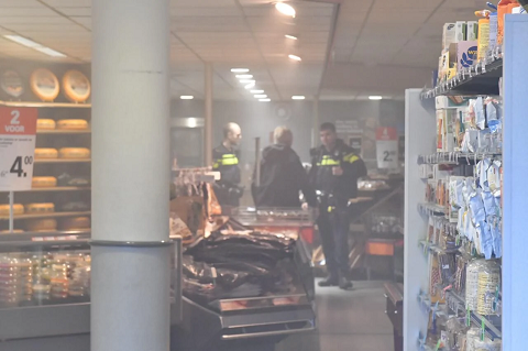 Winkelinterieur met zichtbare rook, politieagenten en een persoon bij een vitrine.