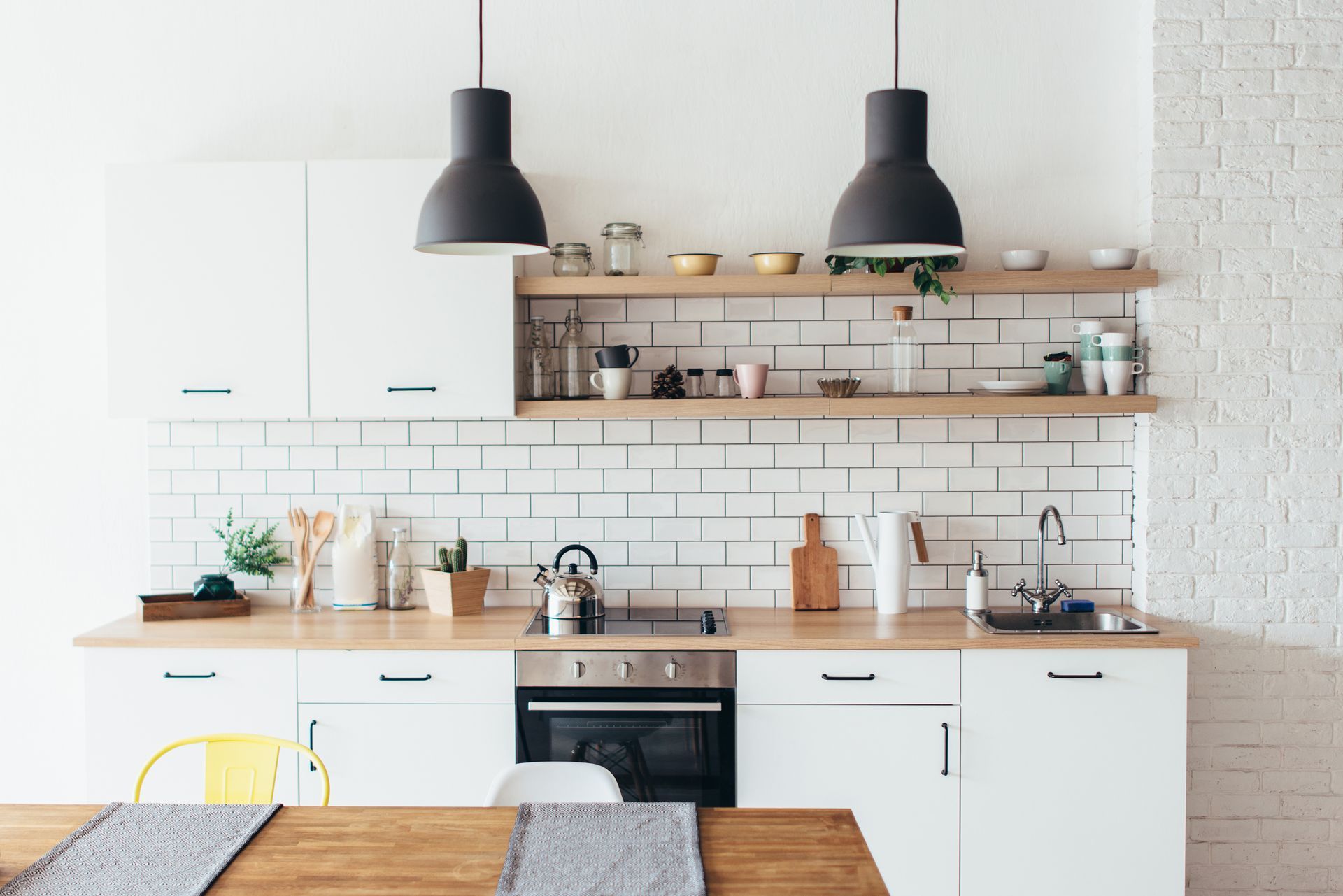 Modern kitchen with white cabinets, wooden countertops, and floating shelves; two black pendant lights hang above.