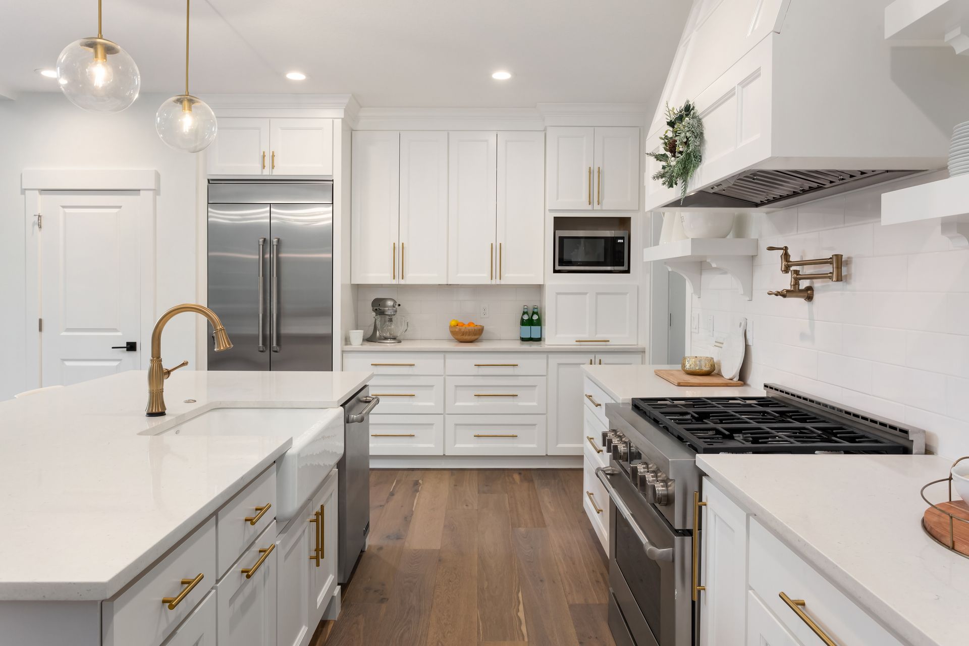 White kitchen with island, stainless steel appliances, and wooden floor.