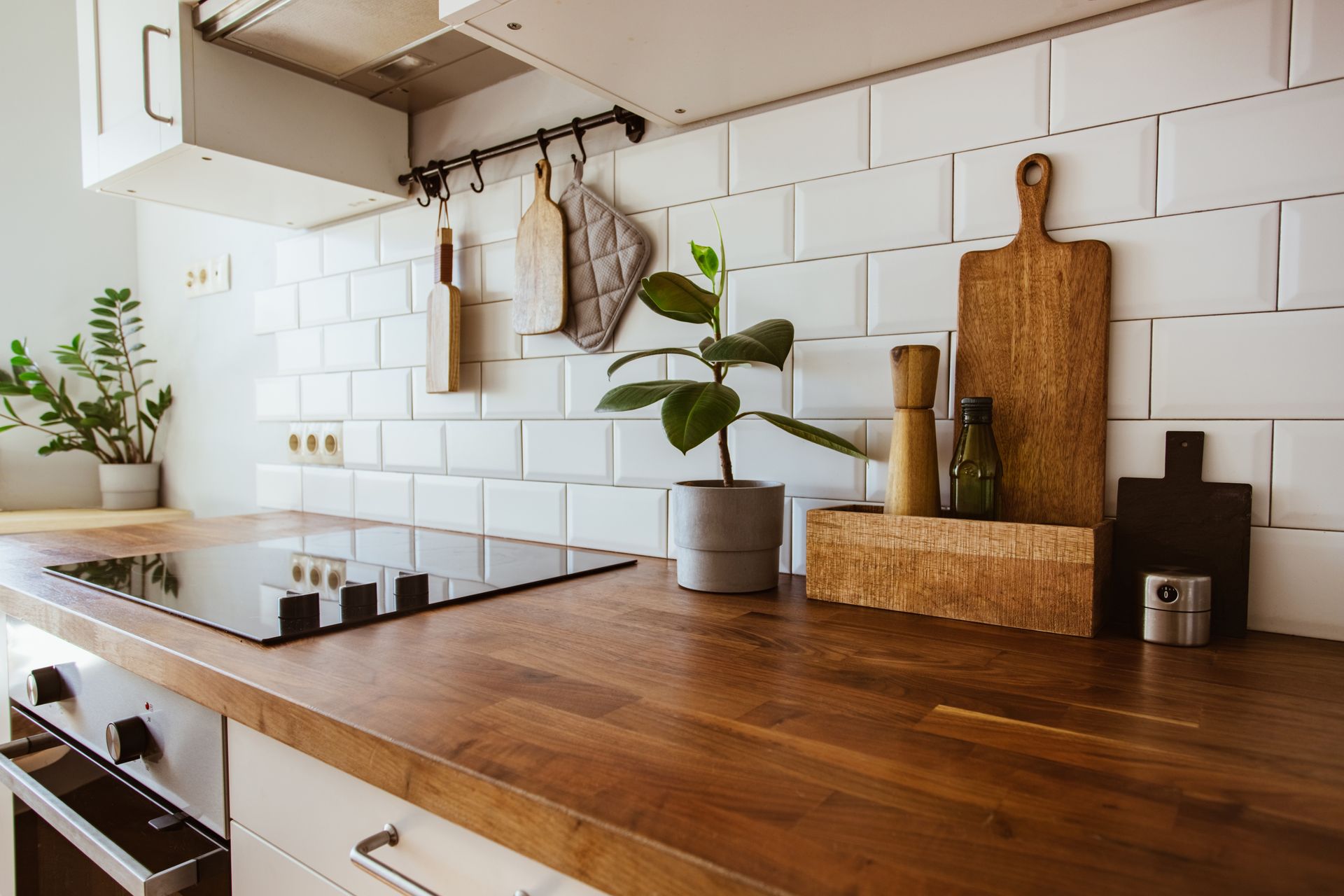 Wooden countertop with a stovetop and white subway tile backsplash, featuring a plant, cutting boards, and utensils.