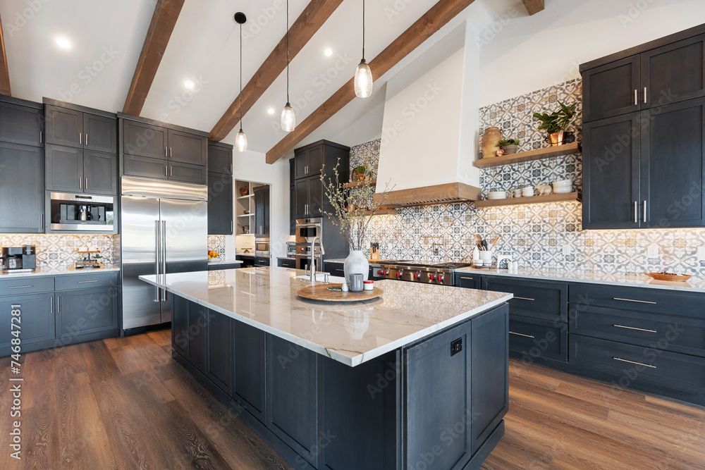 Modern kitchen with dark blue cabinets, large island, wood beams, and patterned backsplash.