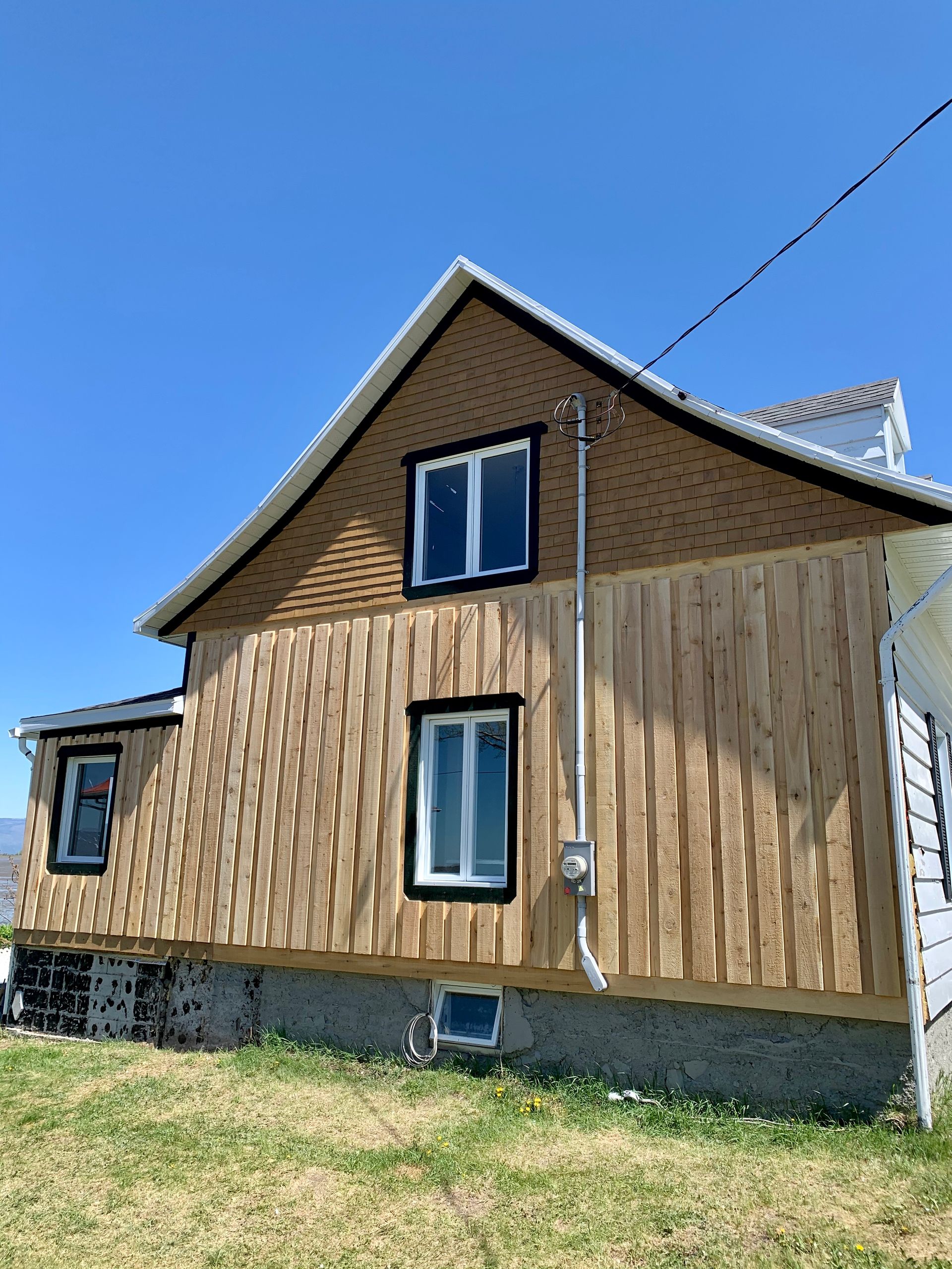 Une maison avec un revêtement en bois et des fenêtres se trouve au milieu d'un champ herbeux.