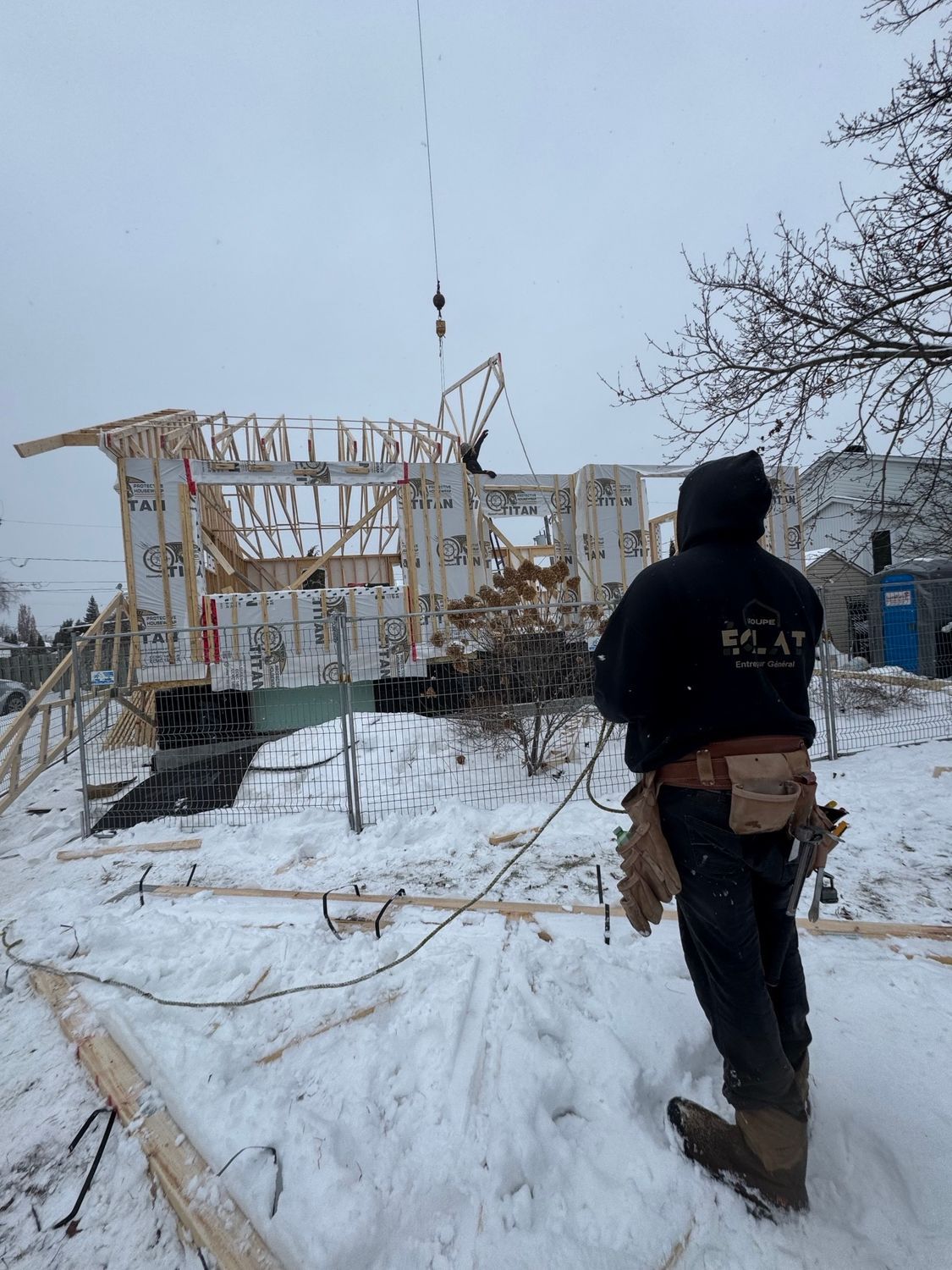 Un homme se tient debout dans la neige devant une maison en construction.