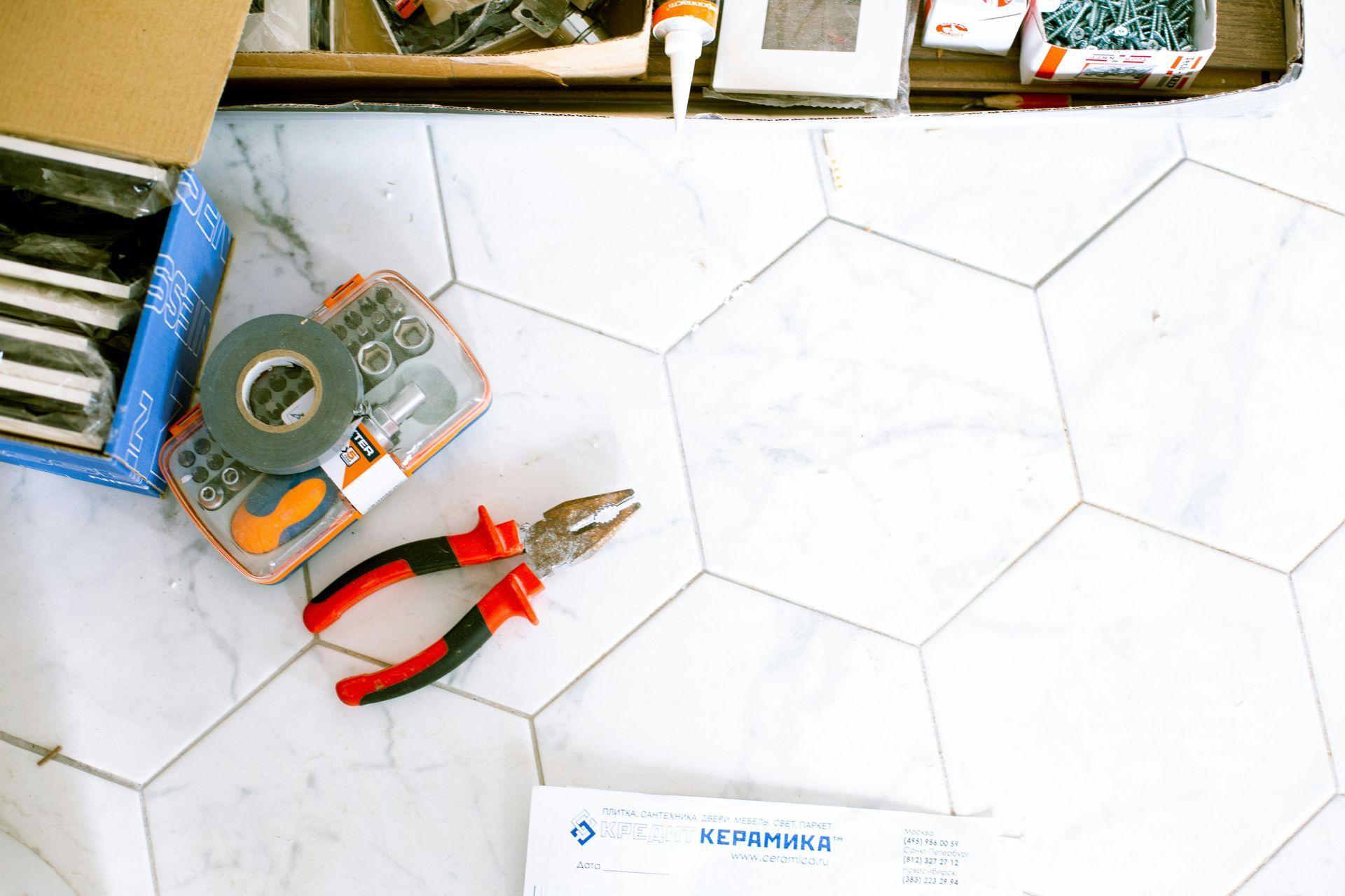Tools (pliers, tape, screwdriver set) on white hexagon tile floor, with an open toolbox.