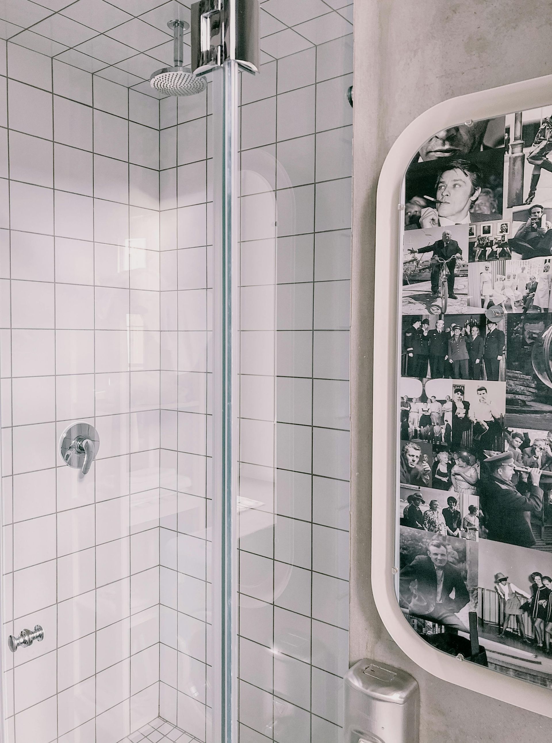 Shower with white tile walls, glass door, chrome fixtures, and collage mirror.