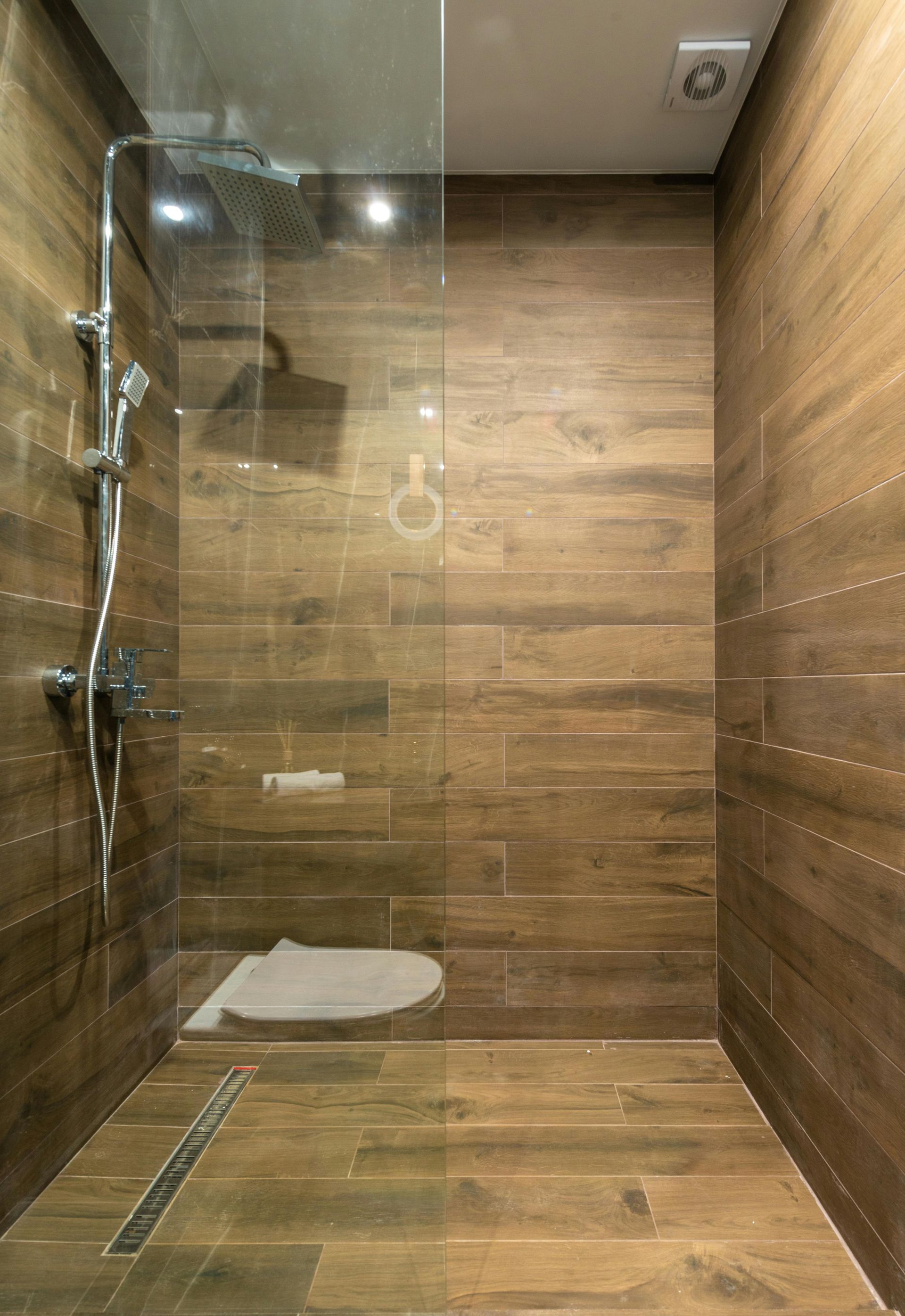 Shower with brown wood-look tiles, glass enclosure, and silver fixtures.
