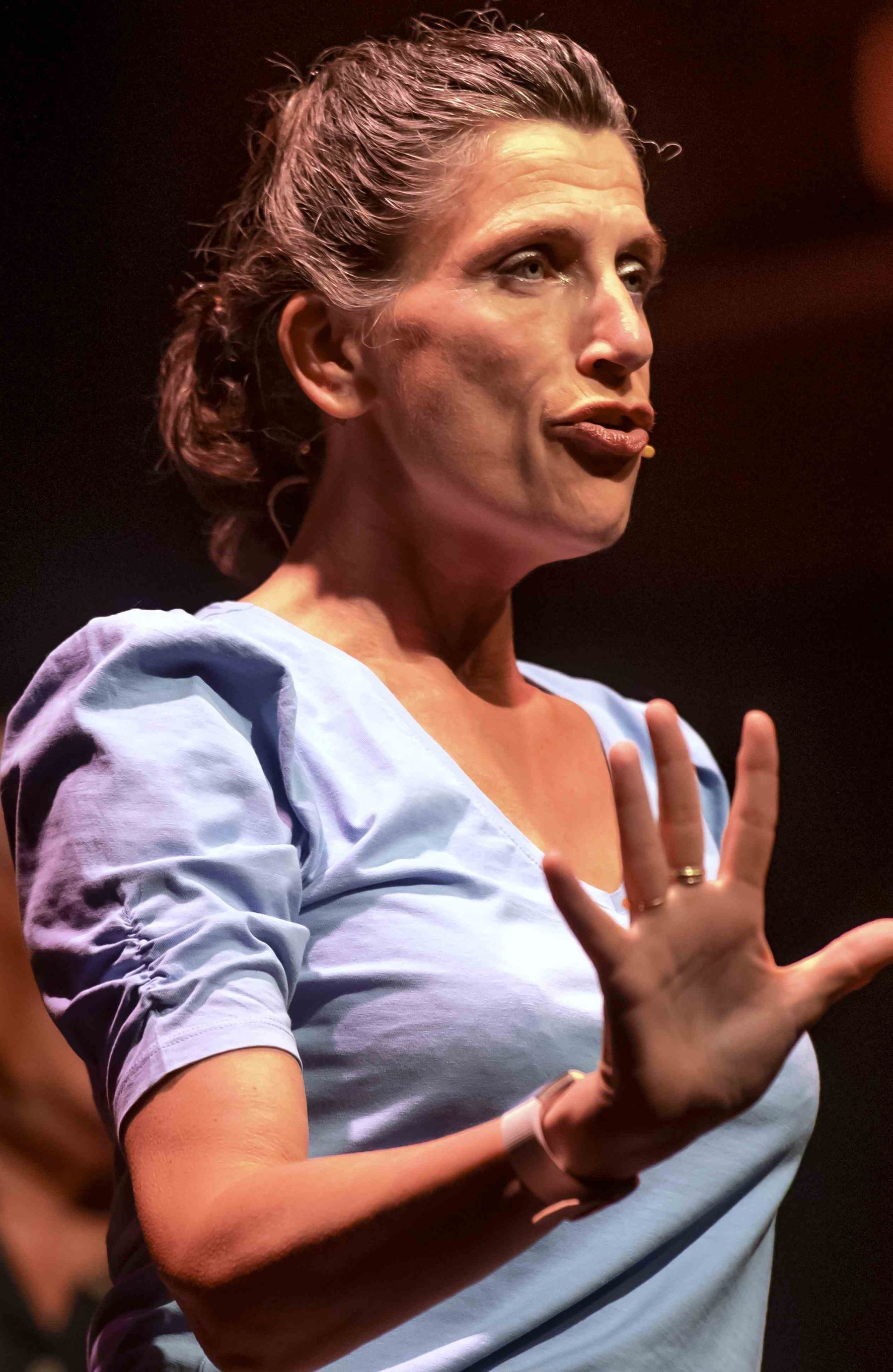 Irene Hemelaar in een blauw shirt maakt een gebaar met haar handen in de Pride Show van Nederlied in Theater Het Zonnehuis