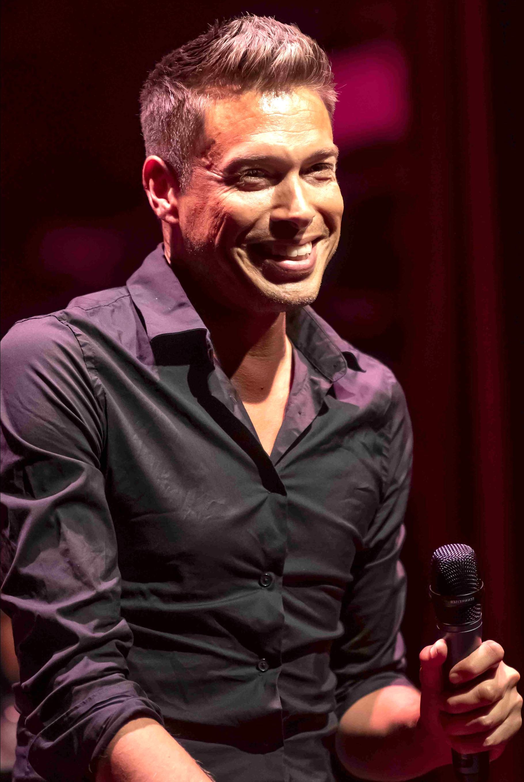 Sjors van der Panne is een zanger. Hij draagt ​​een paars overhemd. Sjors is te zien in de Pride Show van Nederlied in theater Het Zonnehuis in Amsterdam.