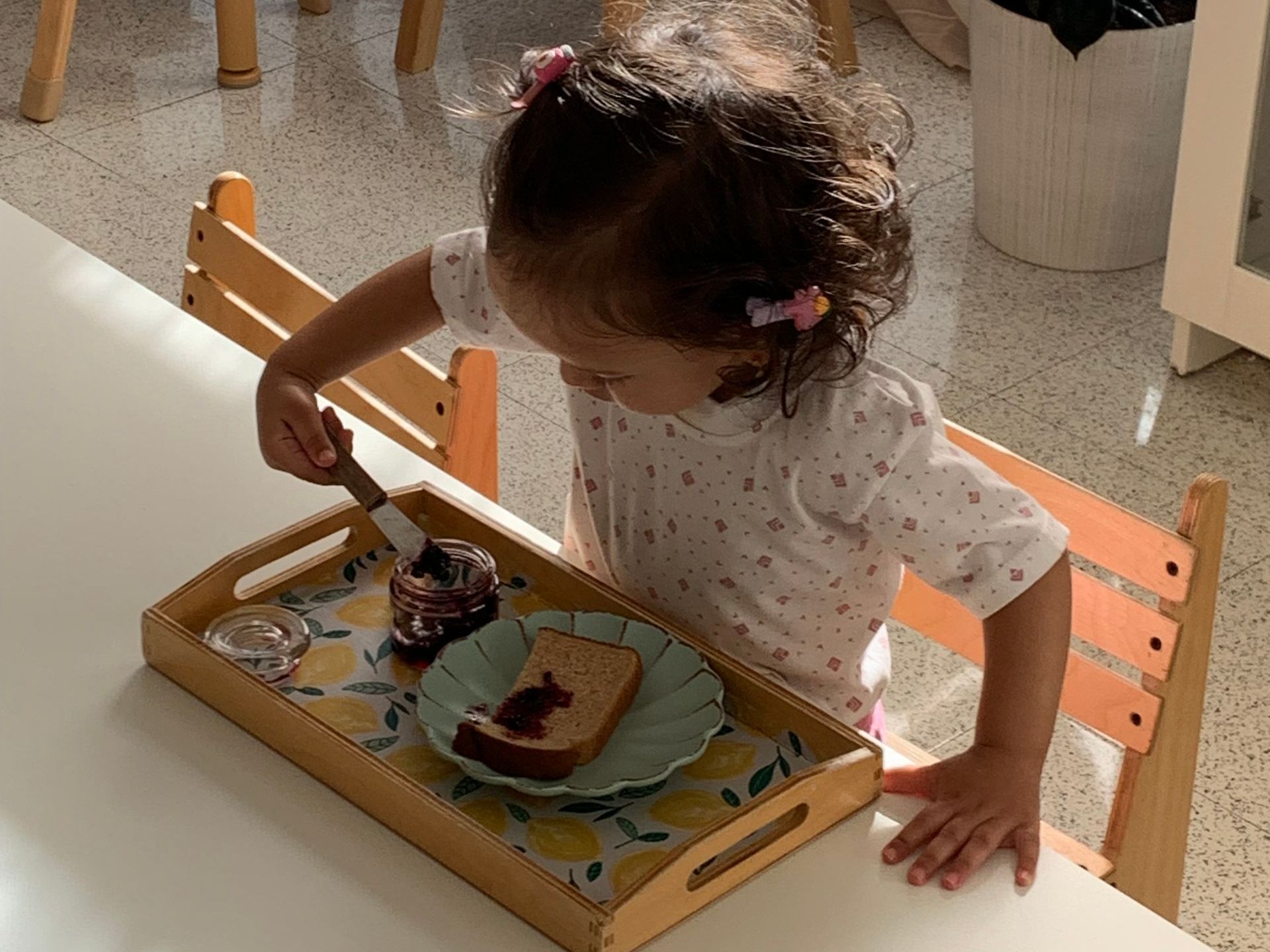 A child spreading jam on toast, a Montessori practical life skill that can be used in the classroom, home, and beyond. This emphasis on independence gives children a tremendous sense of empowerment.