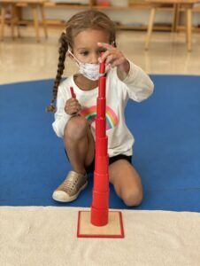 A child deeply concentrated with the knobless cylinders from sensorial