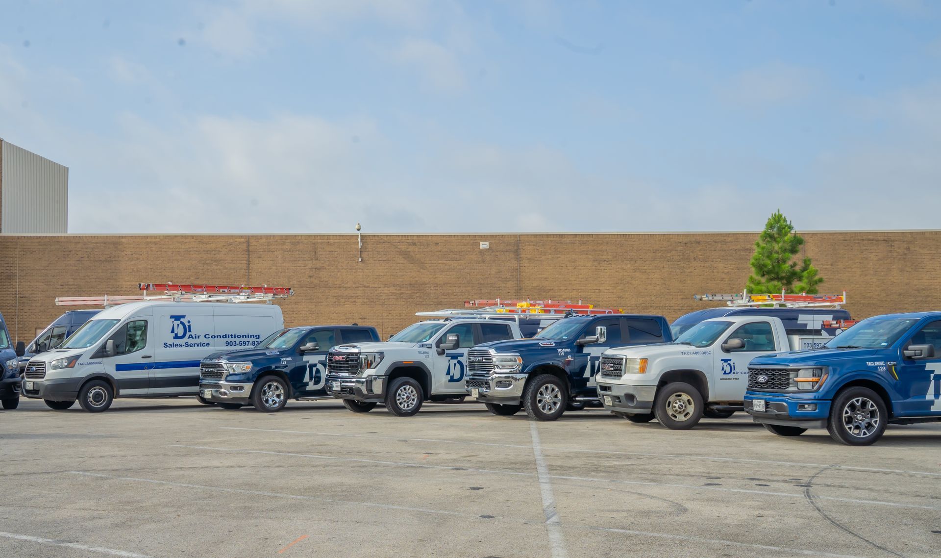 A row of company vehicles parked outdoors against a brick wall on a sunny day.