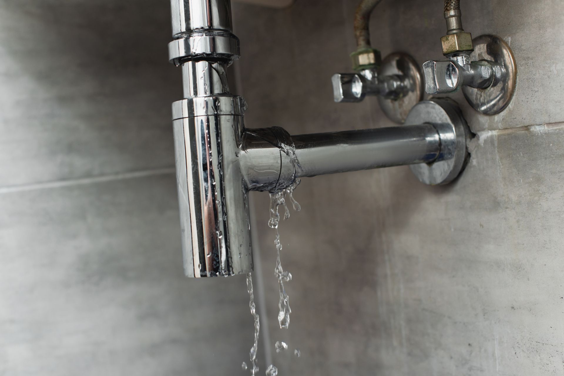 Chrome plumbing pipe leaking water, in a tiled setting.