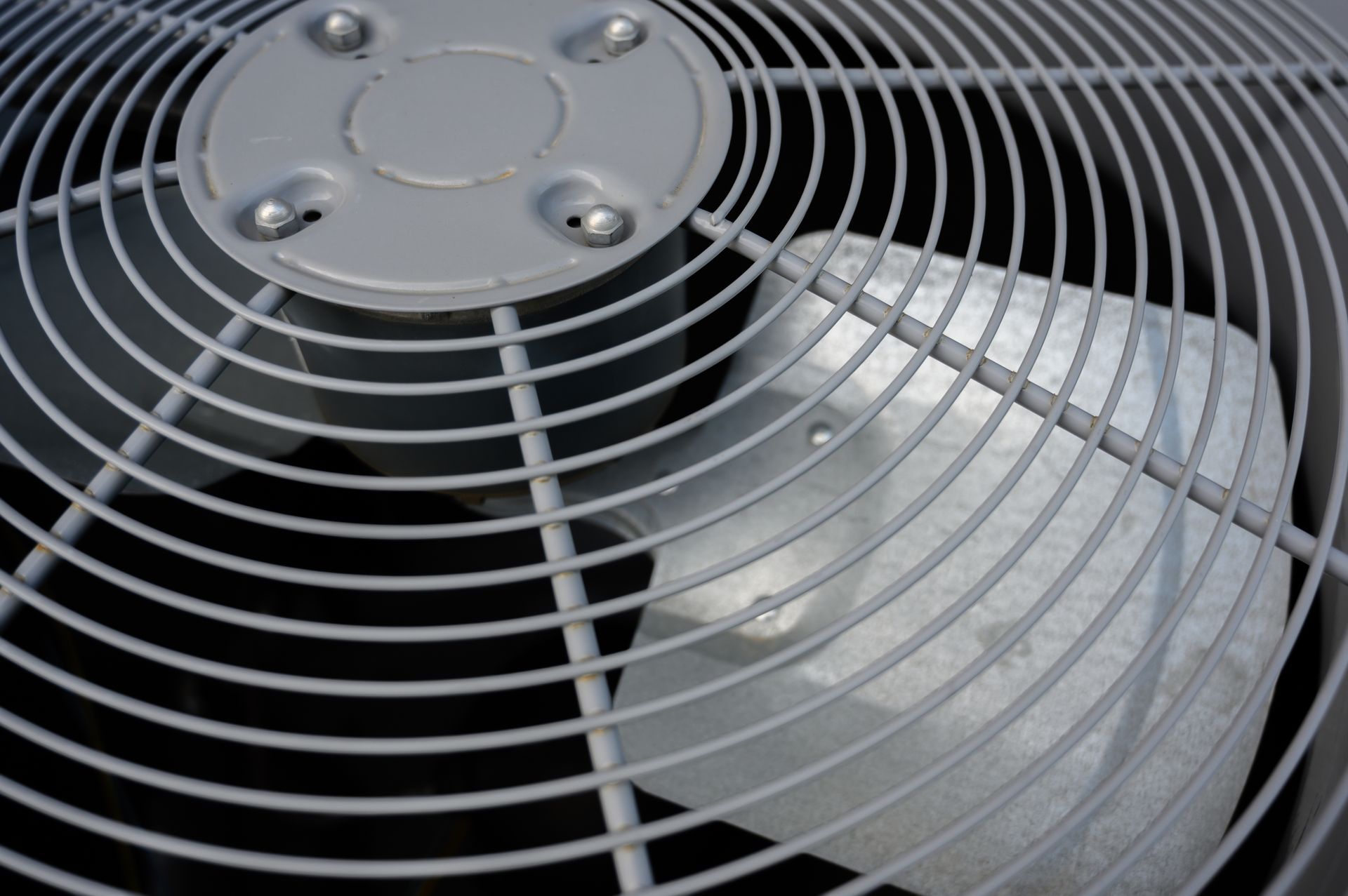Close-up of an air conditioner fan covered by a metal grill, outdoors.
