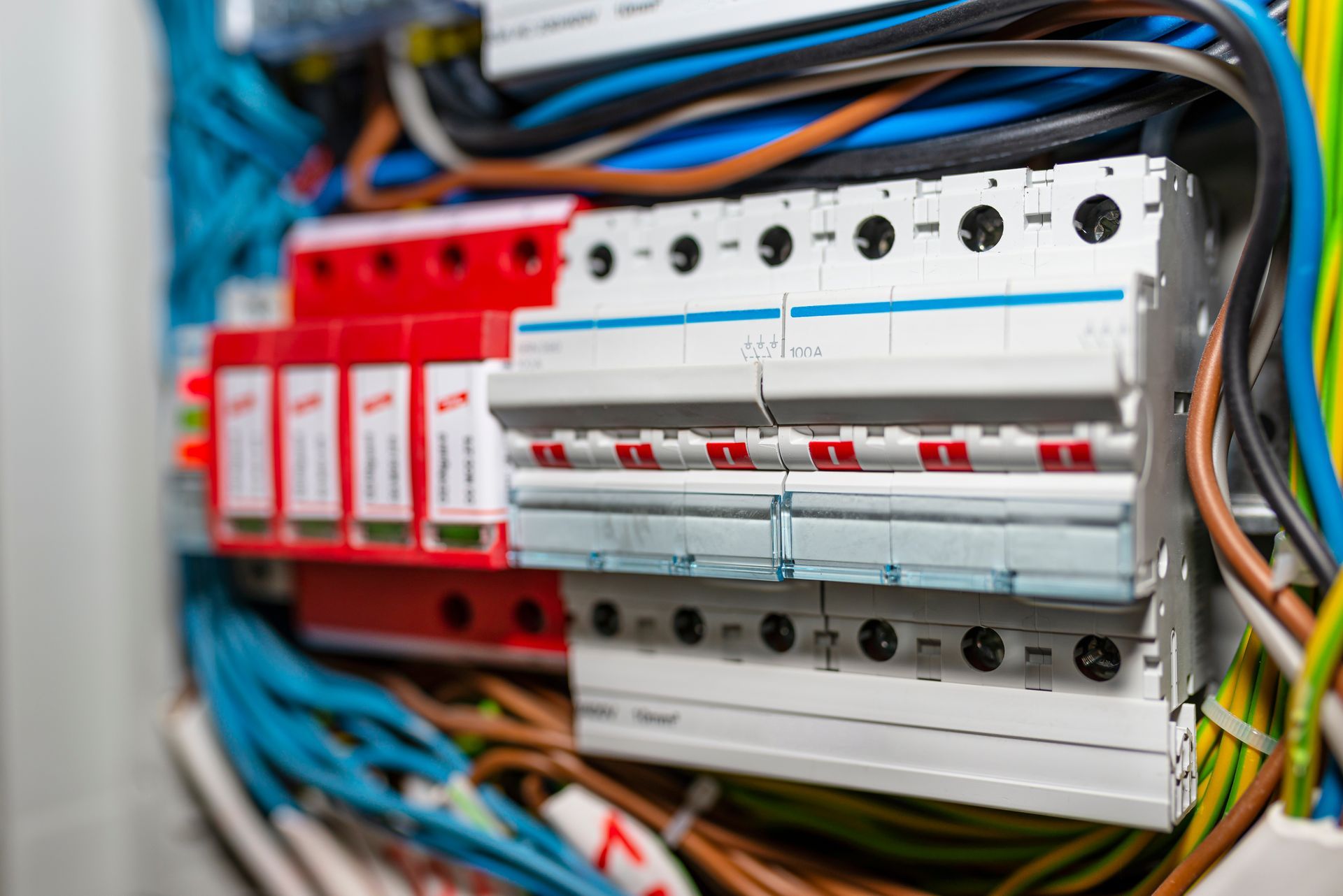 Close-up of a residential electrical panel with colorful wires and red and white circuit breakers.