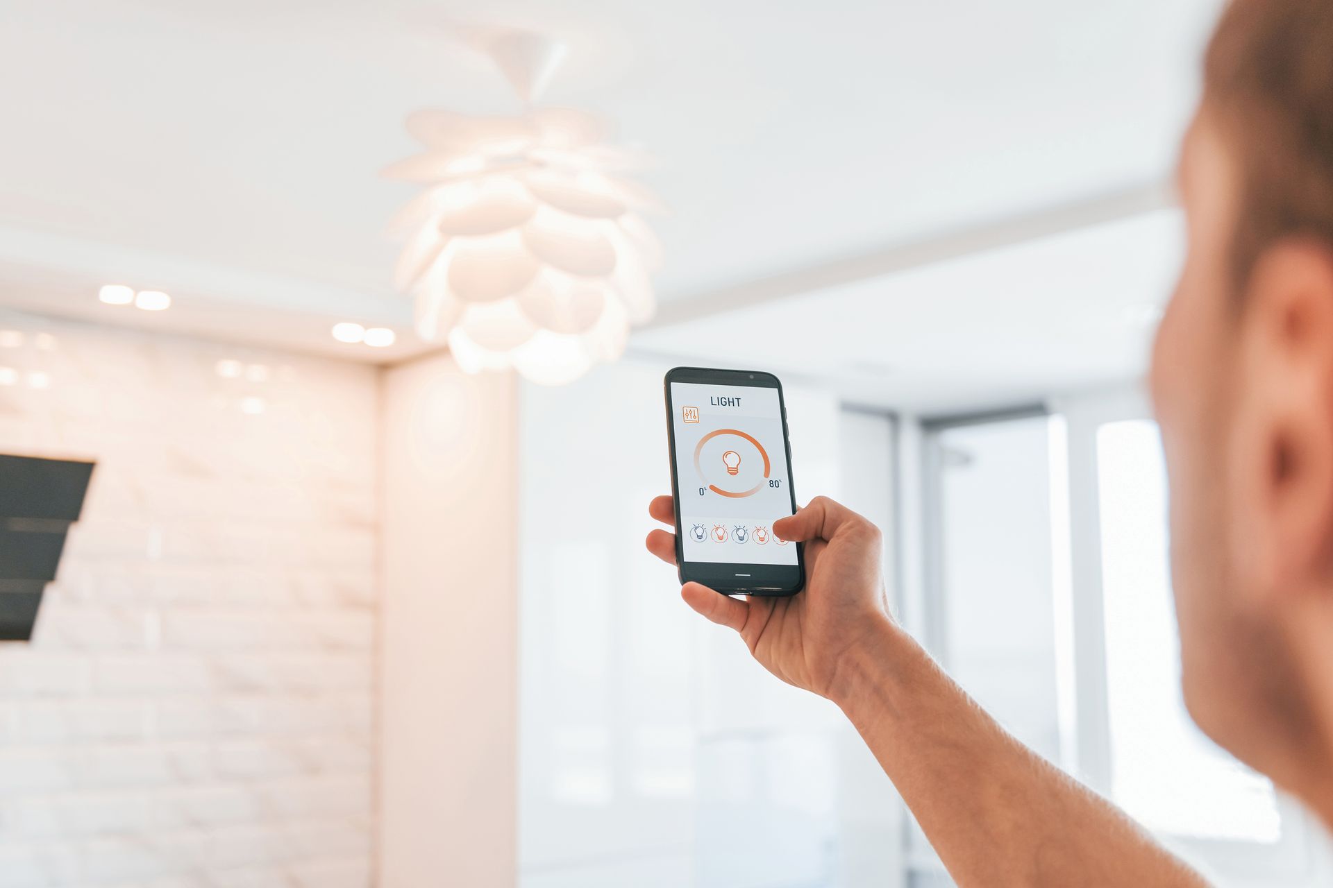 Person holding a smartphone, controlling a light fixture in a modern room.