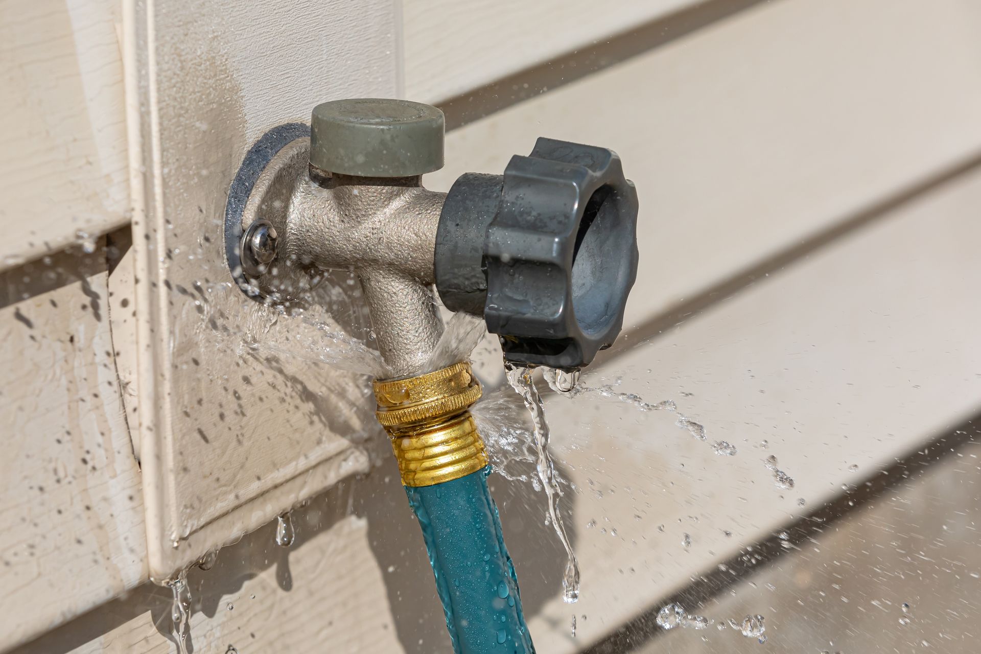 A hand holding a water filter housing. The clear container shows sediment. Blue filter head, metal pipes, and tiled wall.