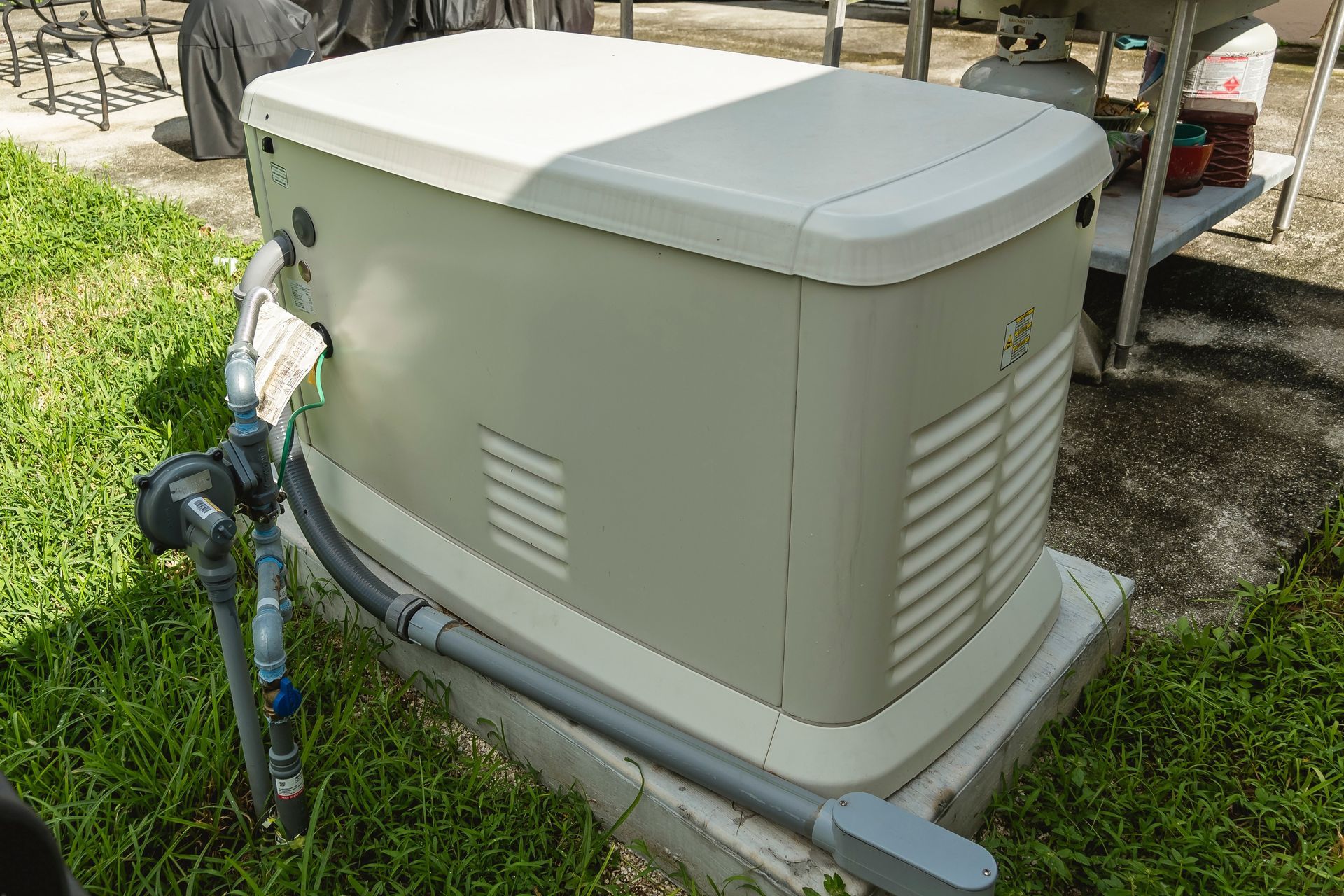 A beige outdoor generator on a concrete base, with a gray conduit and blue water pipe visible in a grassy setting.