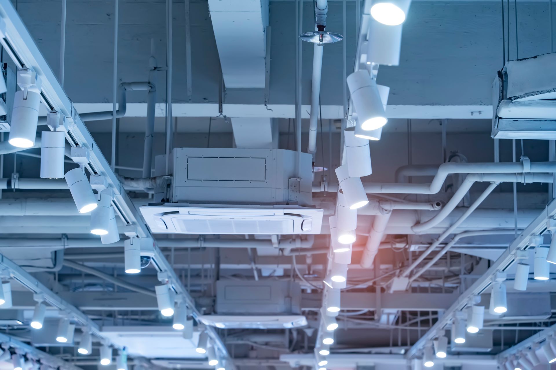 White ceiling with exposed pipes, ducts, and track lighting.