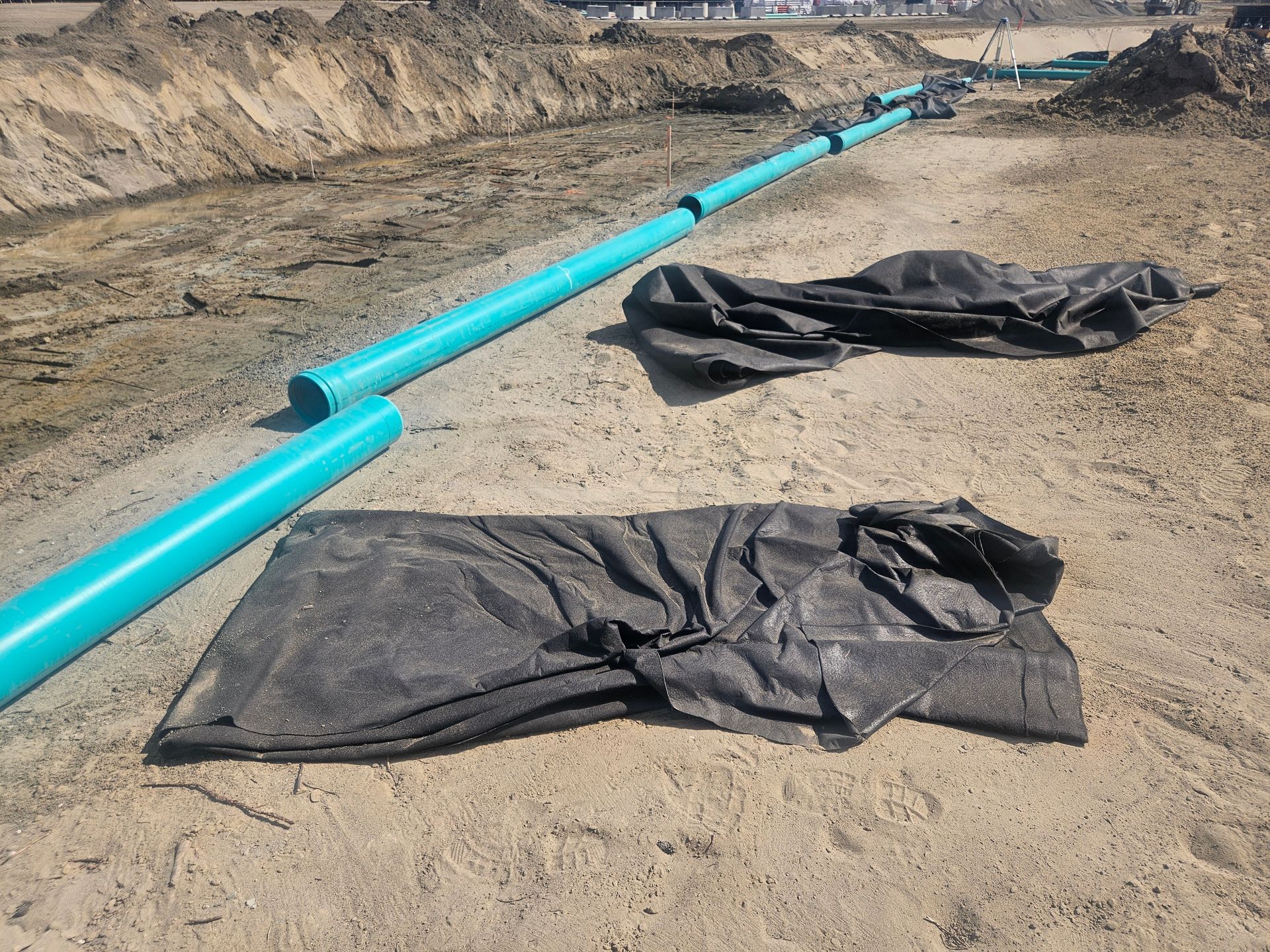 Blue pipes laid in a trench, construction site with black fabric.