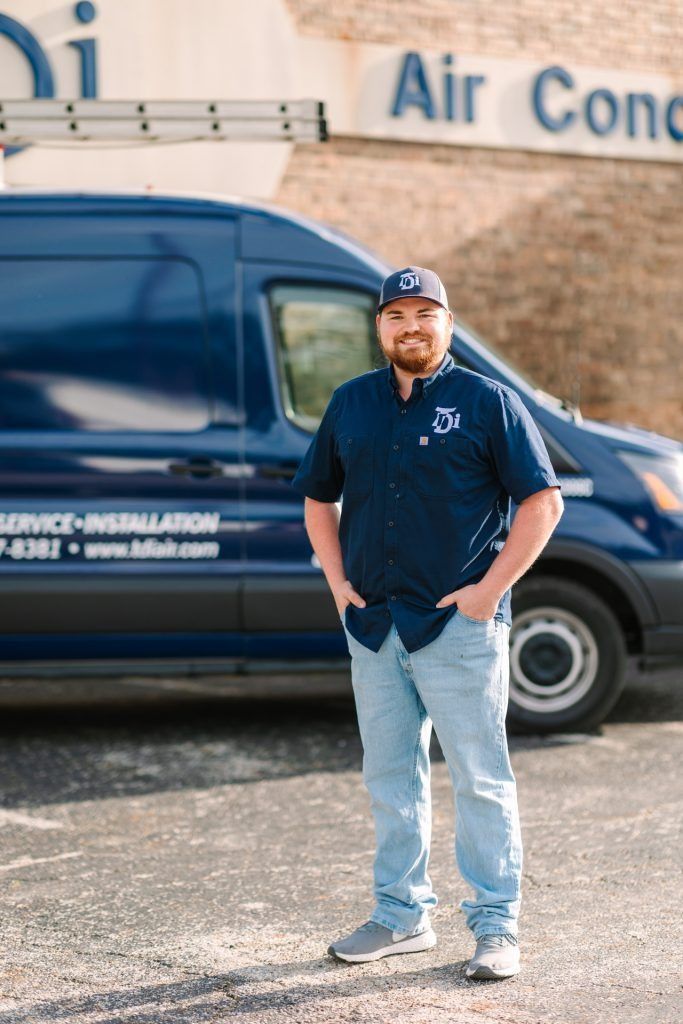 Man in blue shirt and hat stands by blue service van labeled