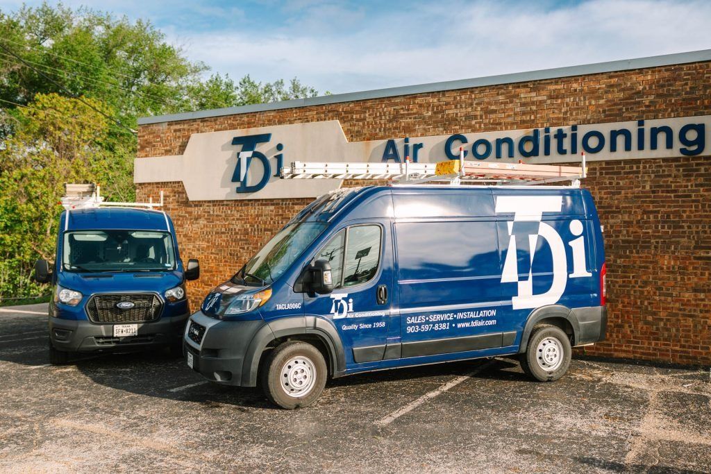 Blue air-conditioning service vans parked outside a brick business sign