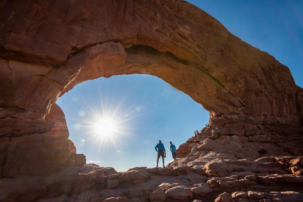 Two people stand under North Window Arch in Arches National Park.