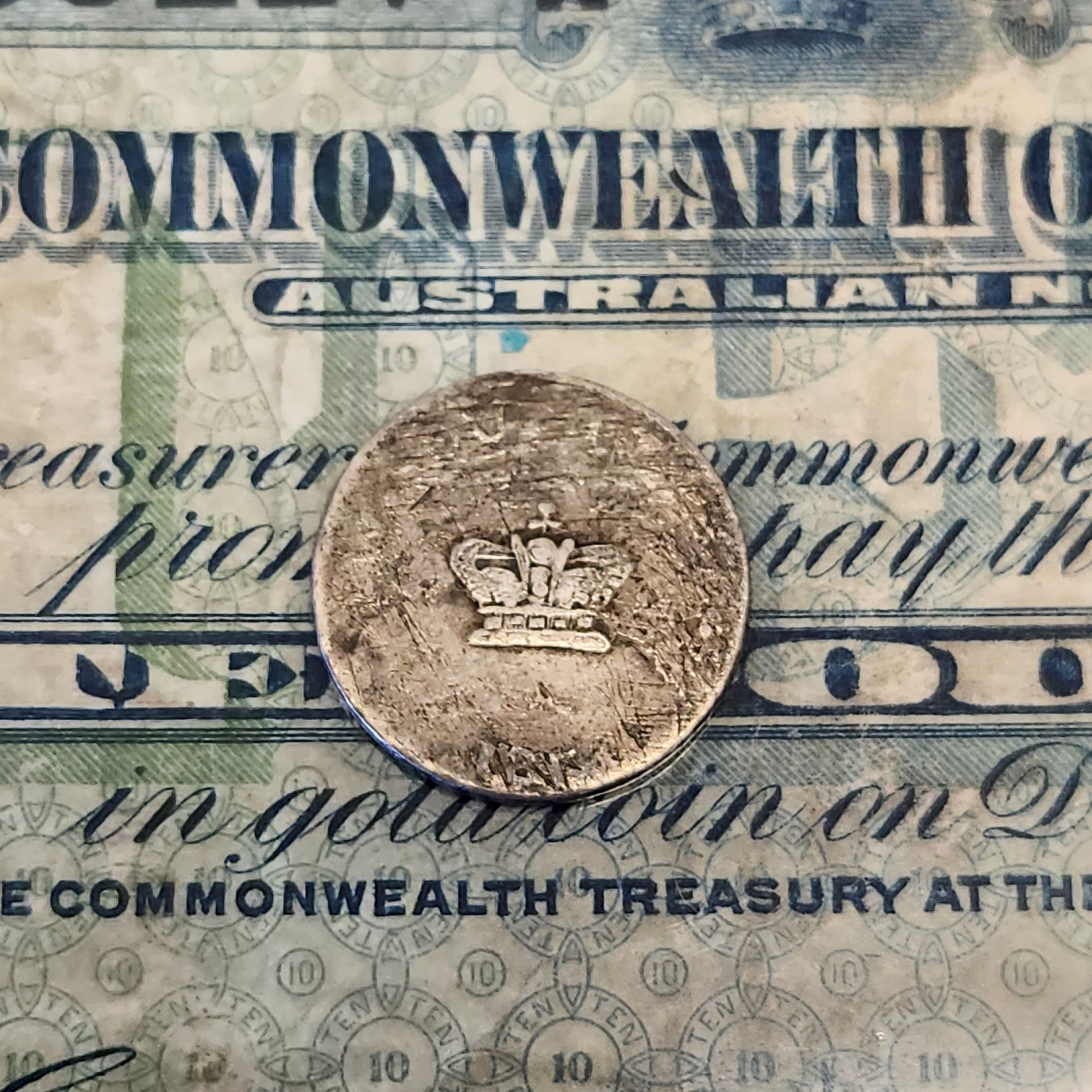 Worn Australian coin featuring crown design placed on a historic Commonwealth of Australia banknote.
