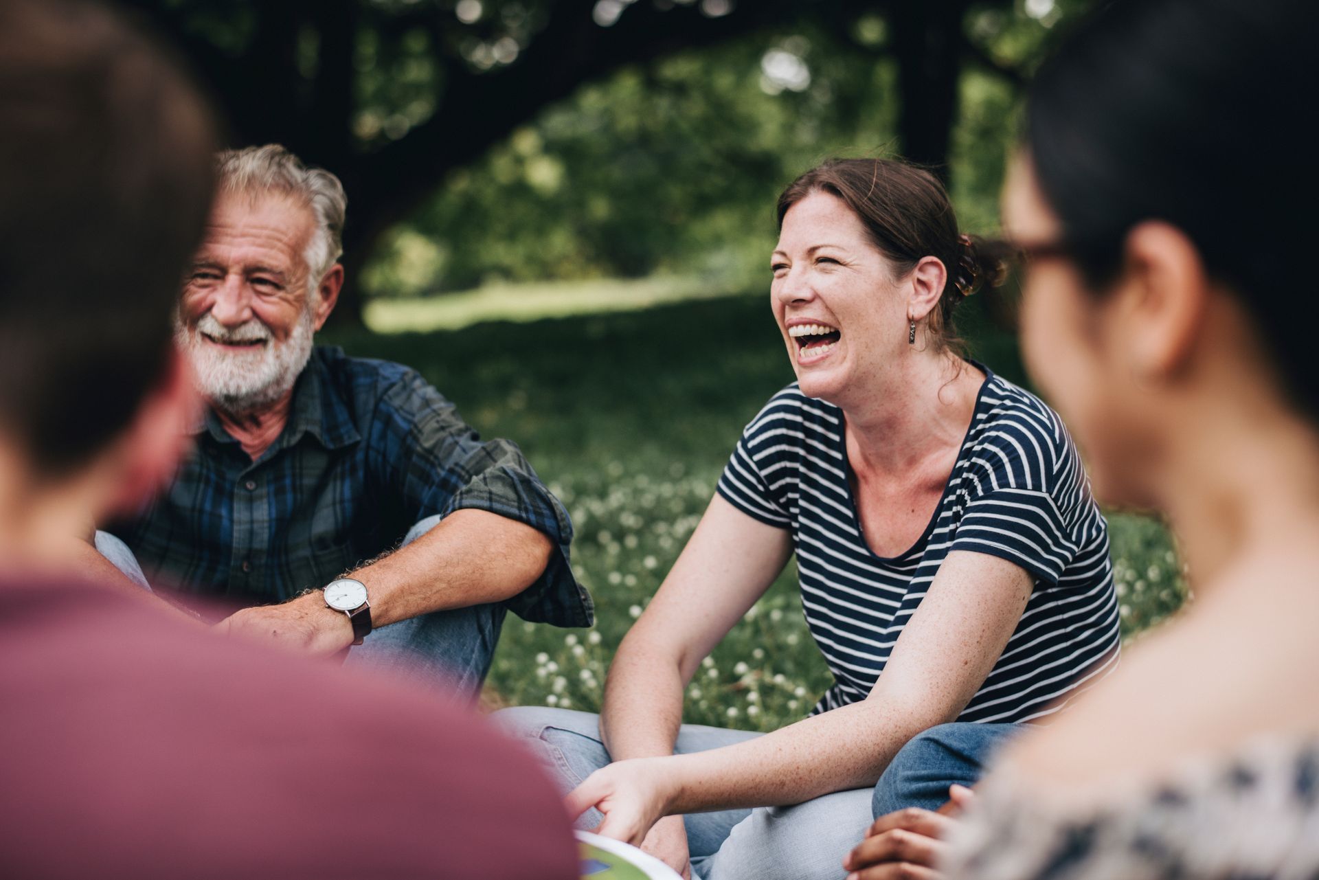 A group of people are sitting in a circle in the grass laughing.