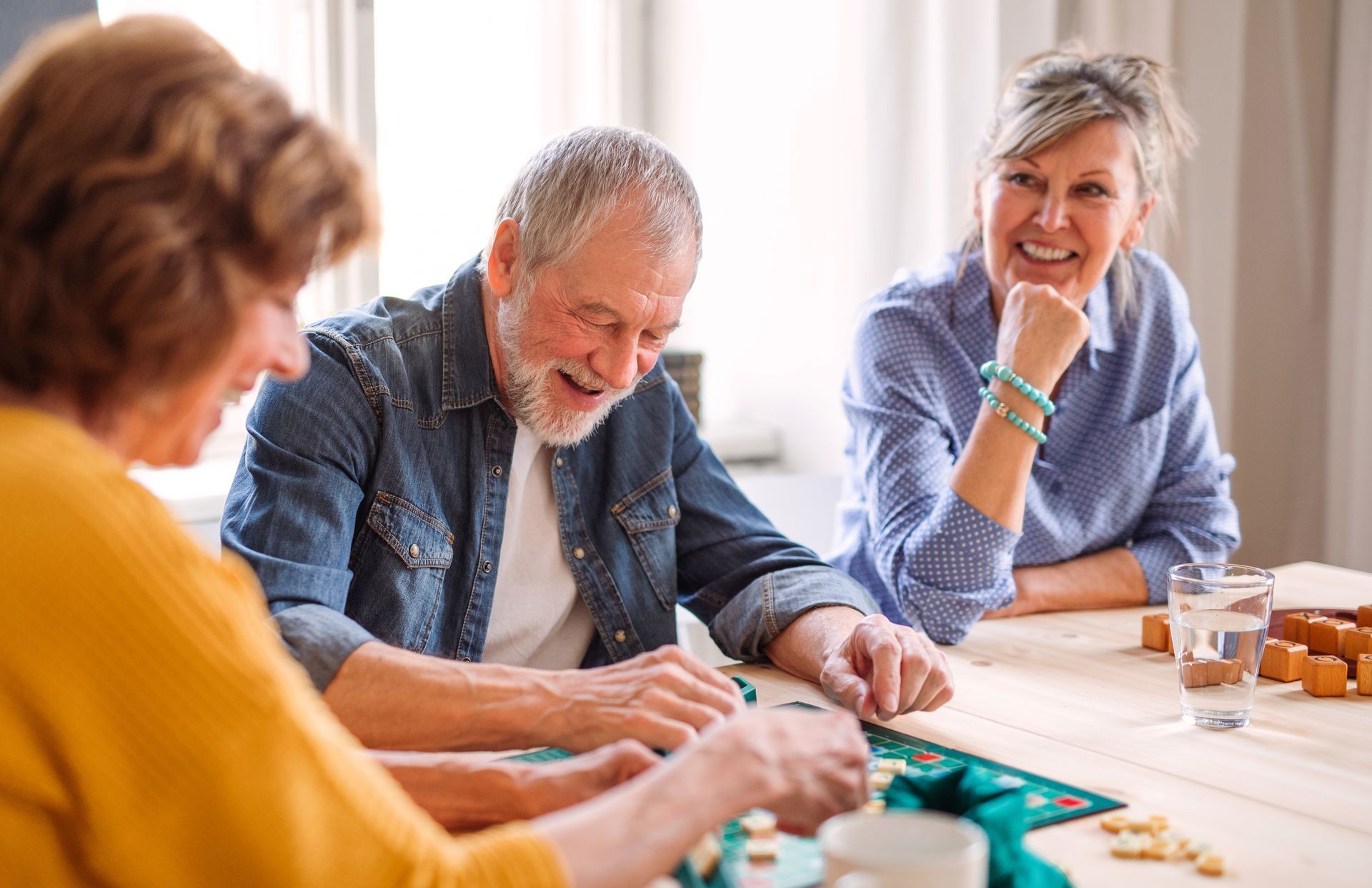 three people playing a board game at a table, smiling and laughing
