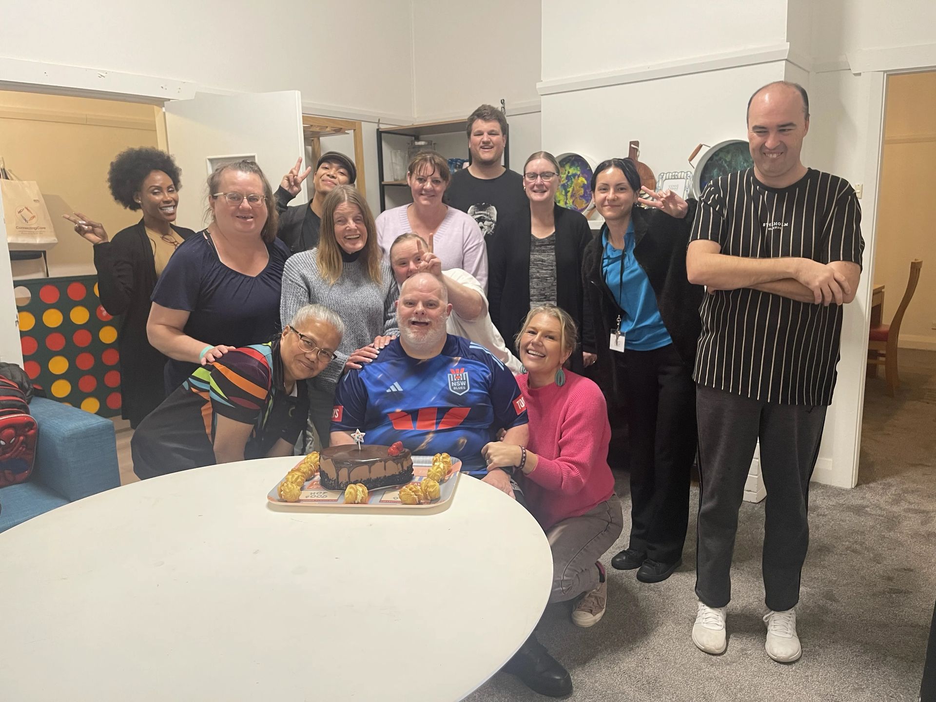 Alive4Life participants and staff gathered around a table celebrating a birthday with a chocolate cake