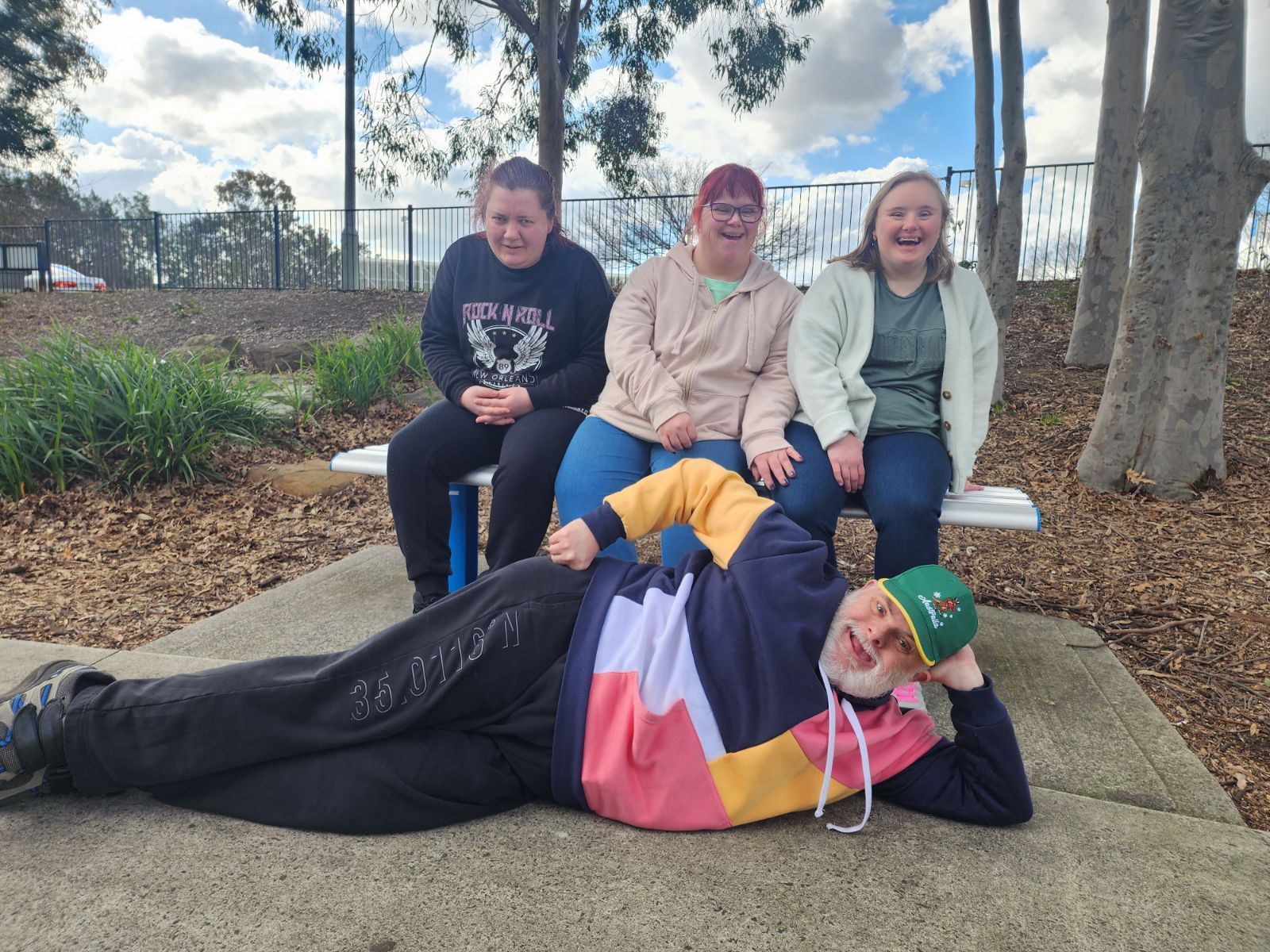 Alive4Life participants relaxing together in the park, with one participant playfully posing on the ground in front