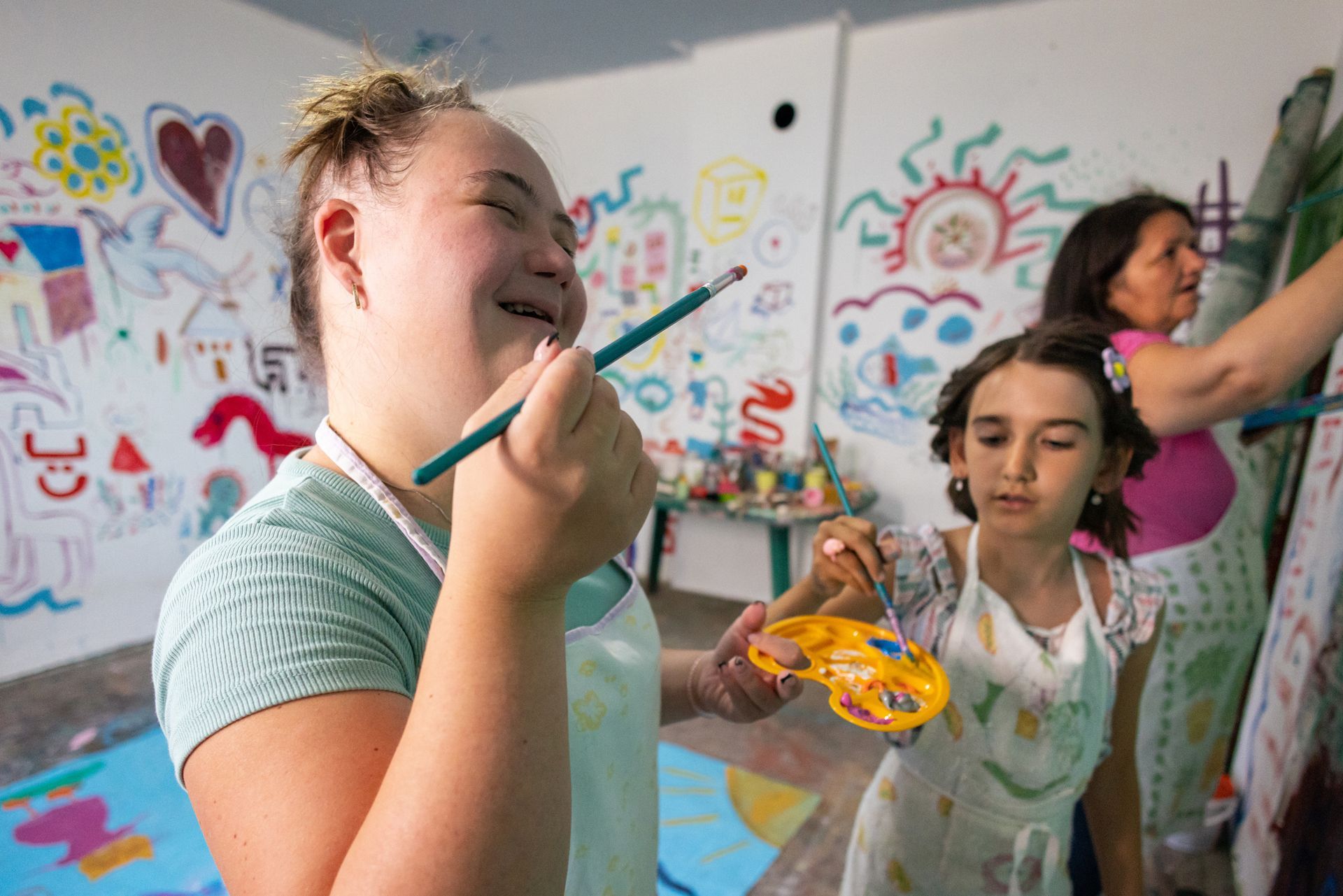Person smiles, painting with others in a brightly decorated art studio.