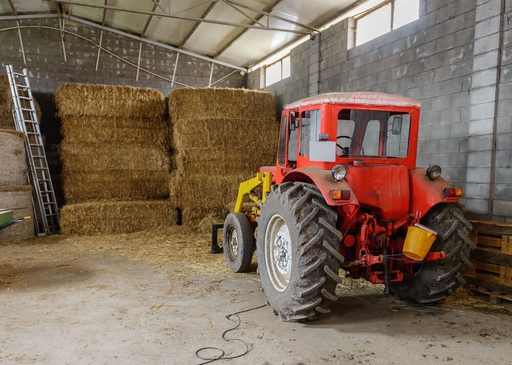 A Red Tractor is Parked in a Barn Filled With Hay Bales — MPE Adventure Quads & Bikes In Thornton, NSW