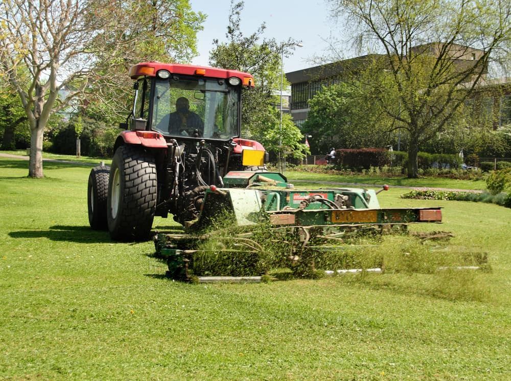 A Red Tractor is Cutting Grass in a Park — MPE Adventure Quads & Bikes In Gosford, NSW