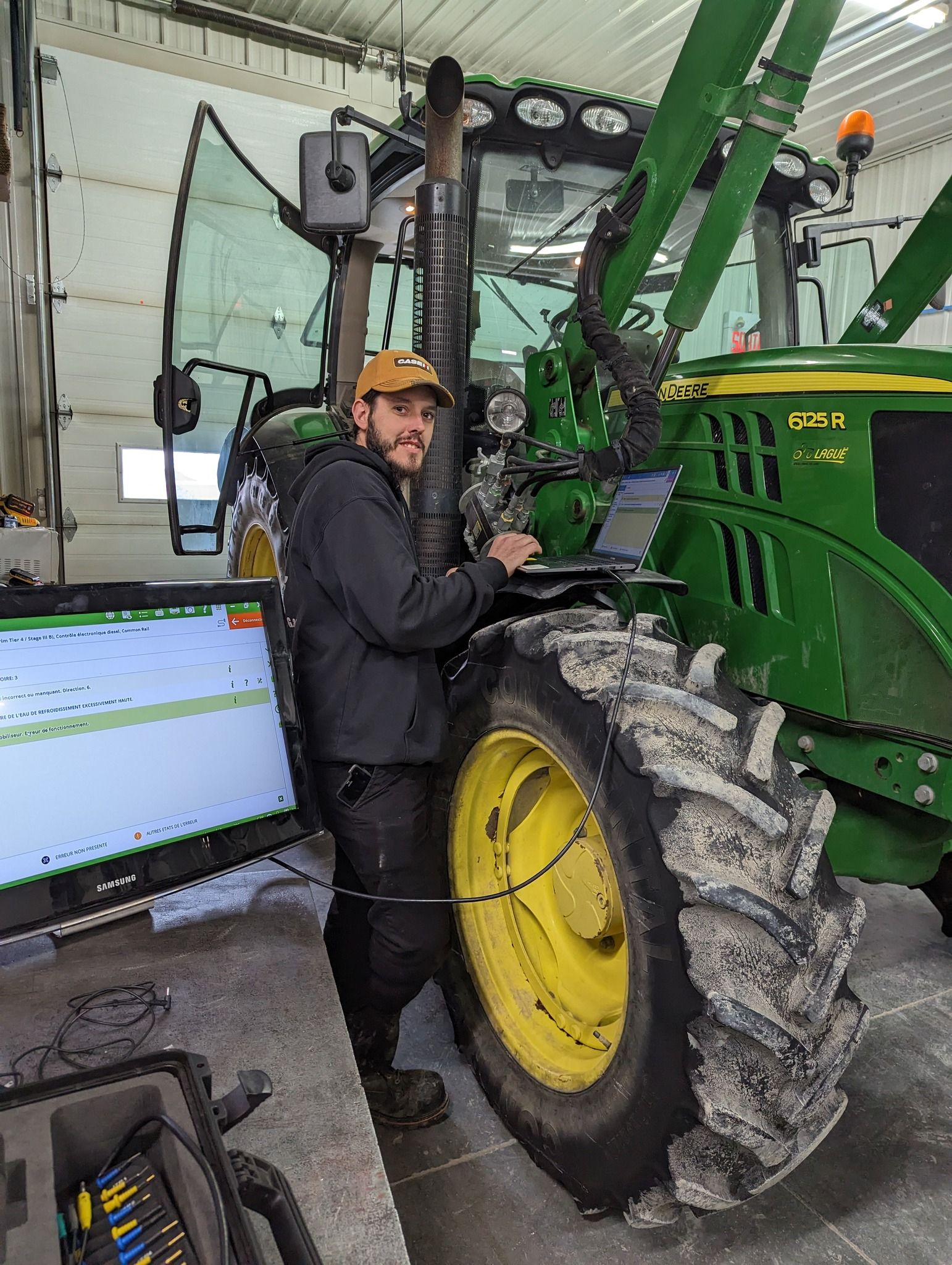 A man is standing next to a green tractor while using a laptop — MPE Adventure Quads & Bikes In Thornton, NSW