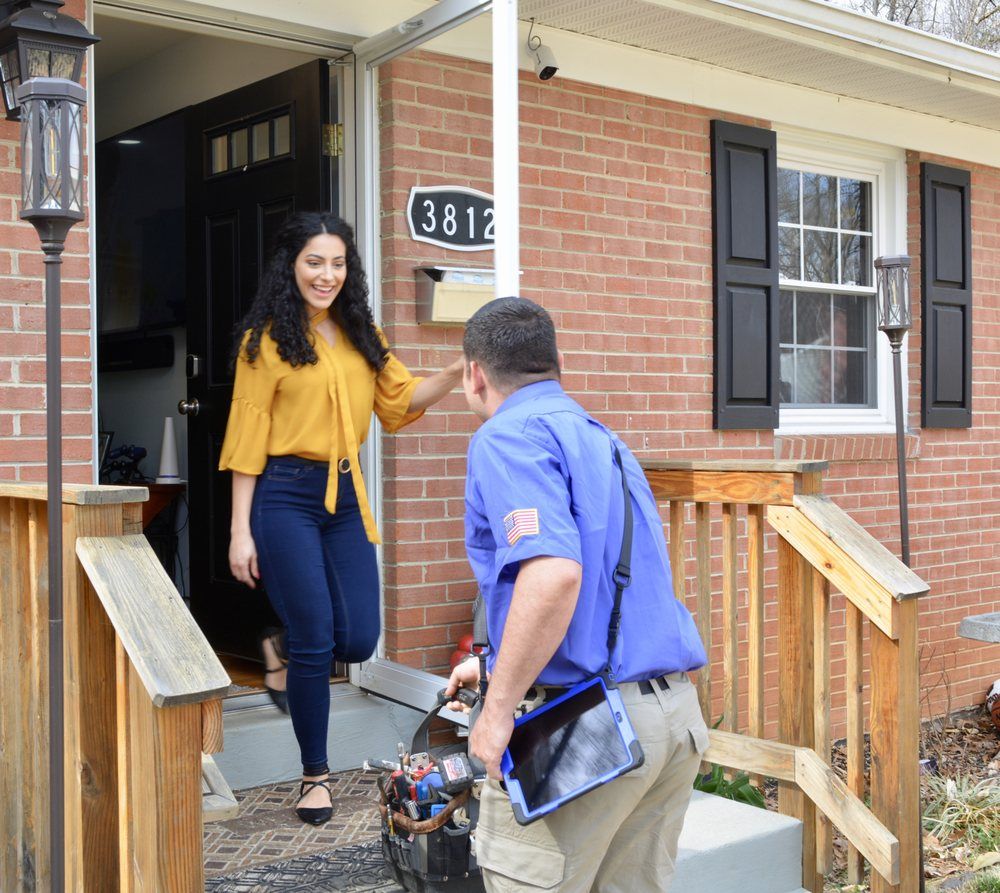 Alex HVAC Service LLC | Woman smiles, greets delivery person at home's front door. House is brick with black shutters.