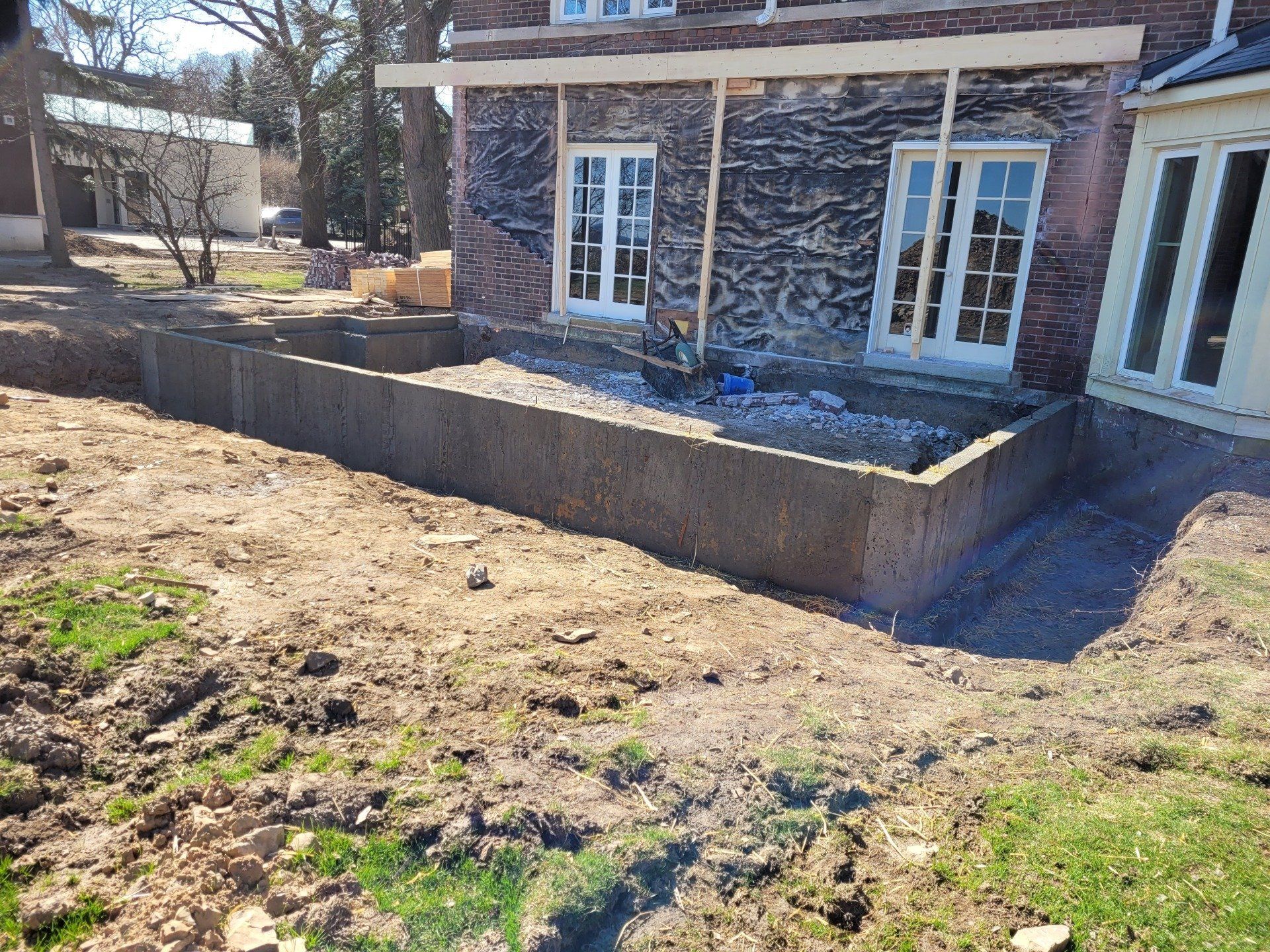 A large concrete wall is being built in front of a brick house.