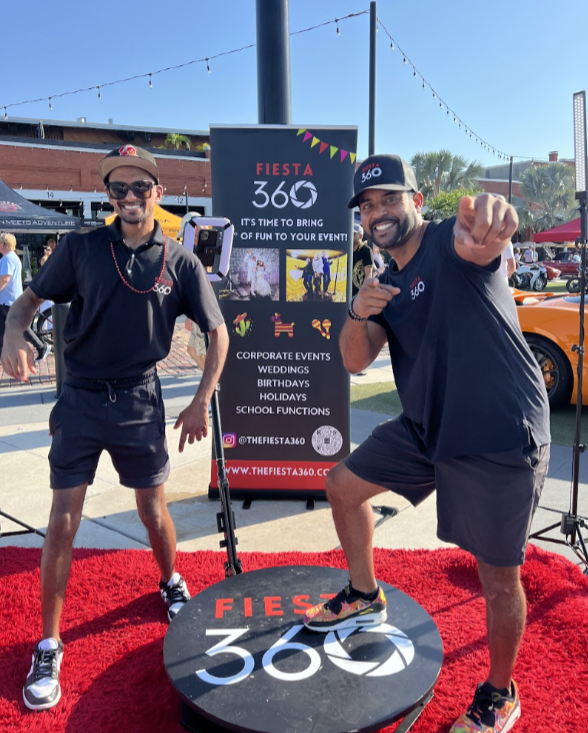Two men standing next to a sign that says fiesta 360
