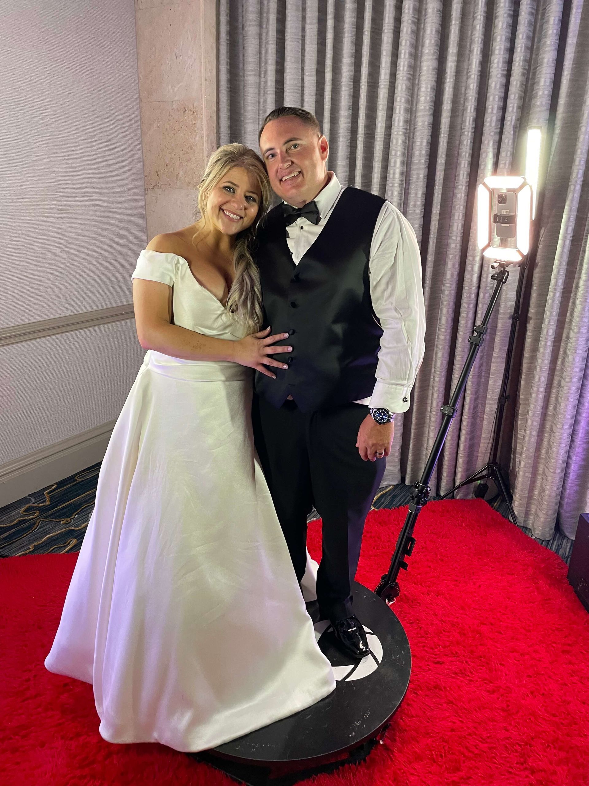 A bride and groom are posing for a picture on a red carpet.