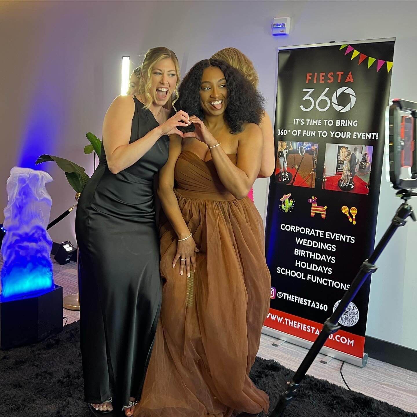 Two women are posing for a picture in front of a sign that says fiesta 360