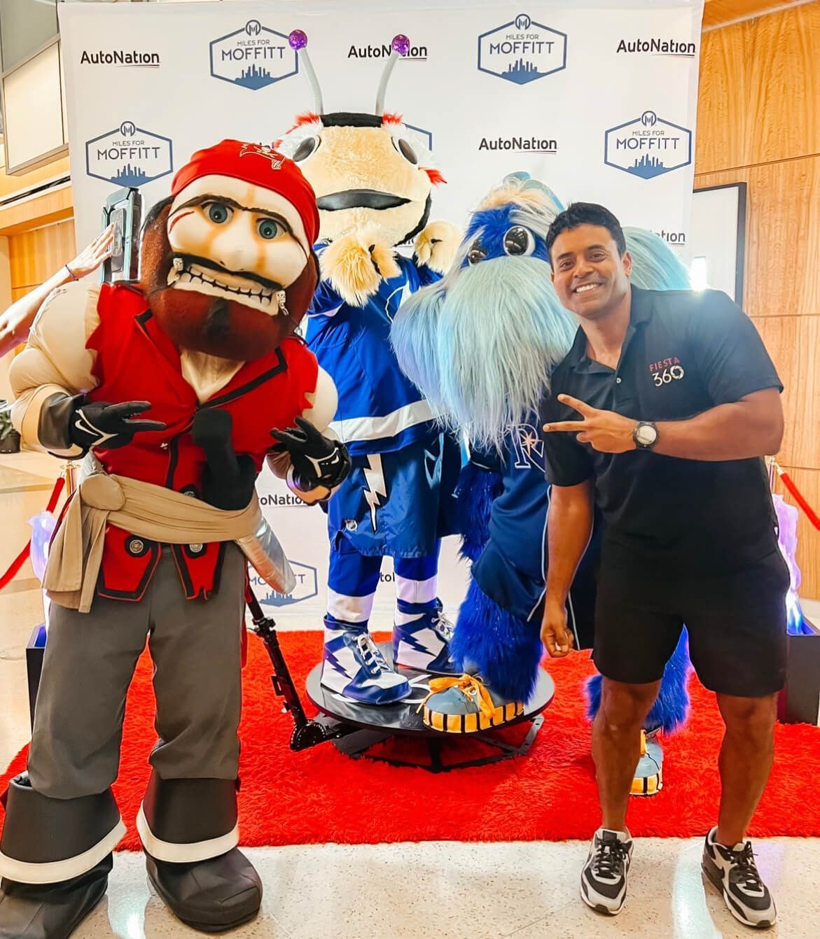 A man is standing next to a mascot on a red carpet.
