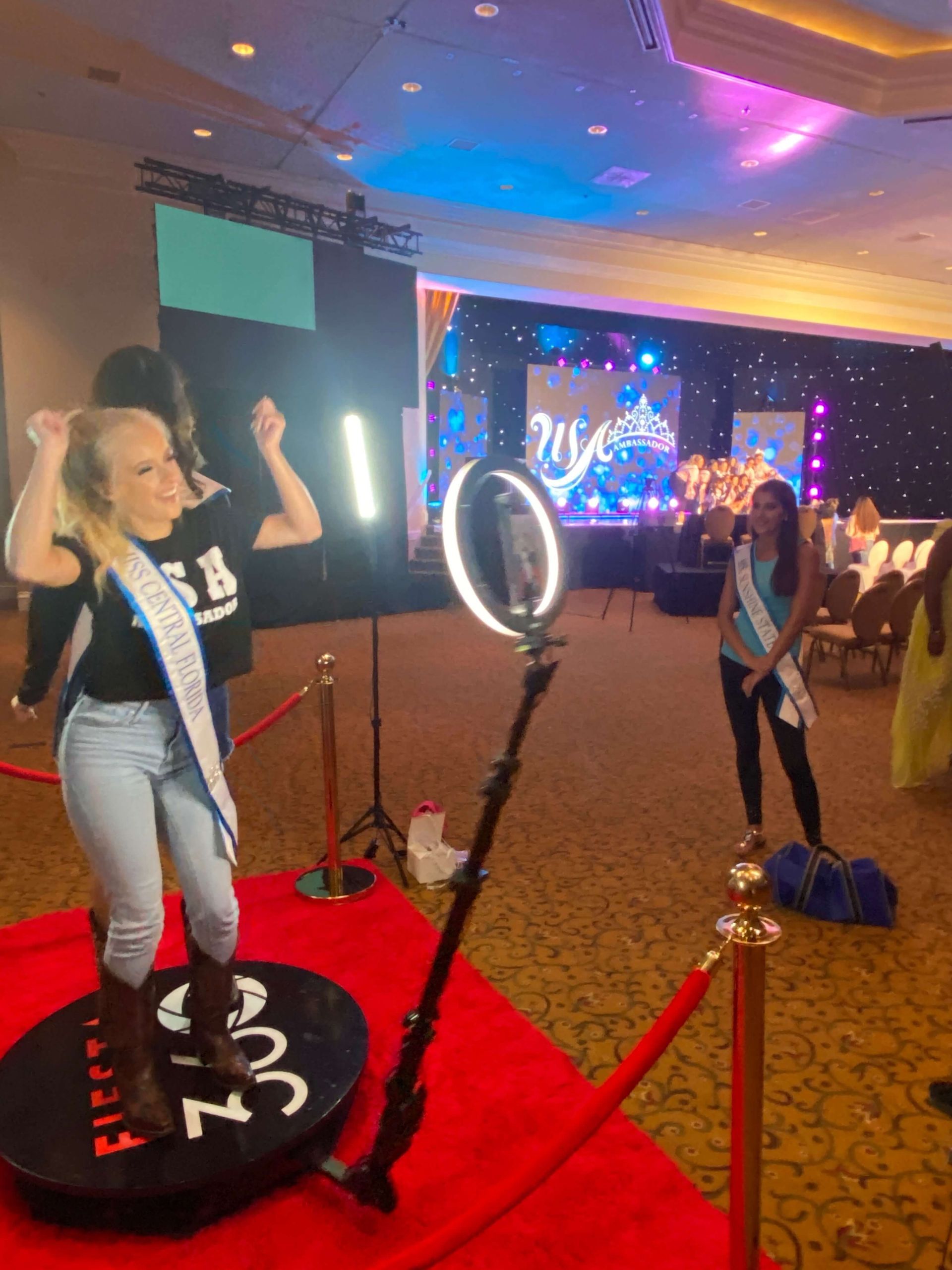 A woman is standing on a red carpet in front of a ring light.