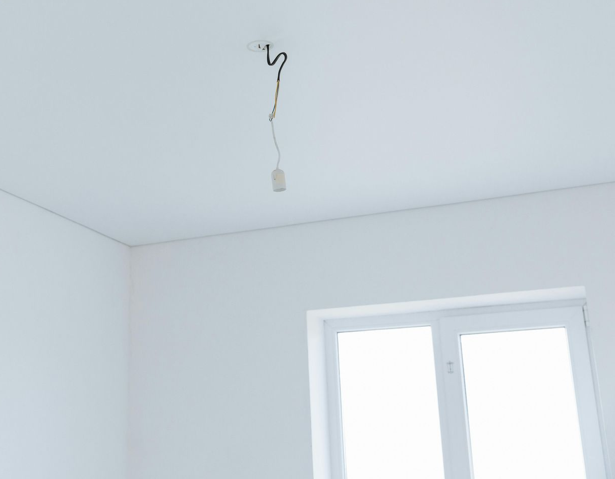 Empty white room with a hanging light fixture and a window on the right