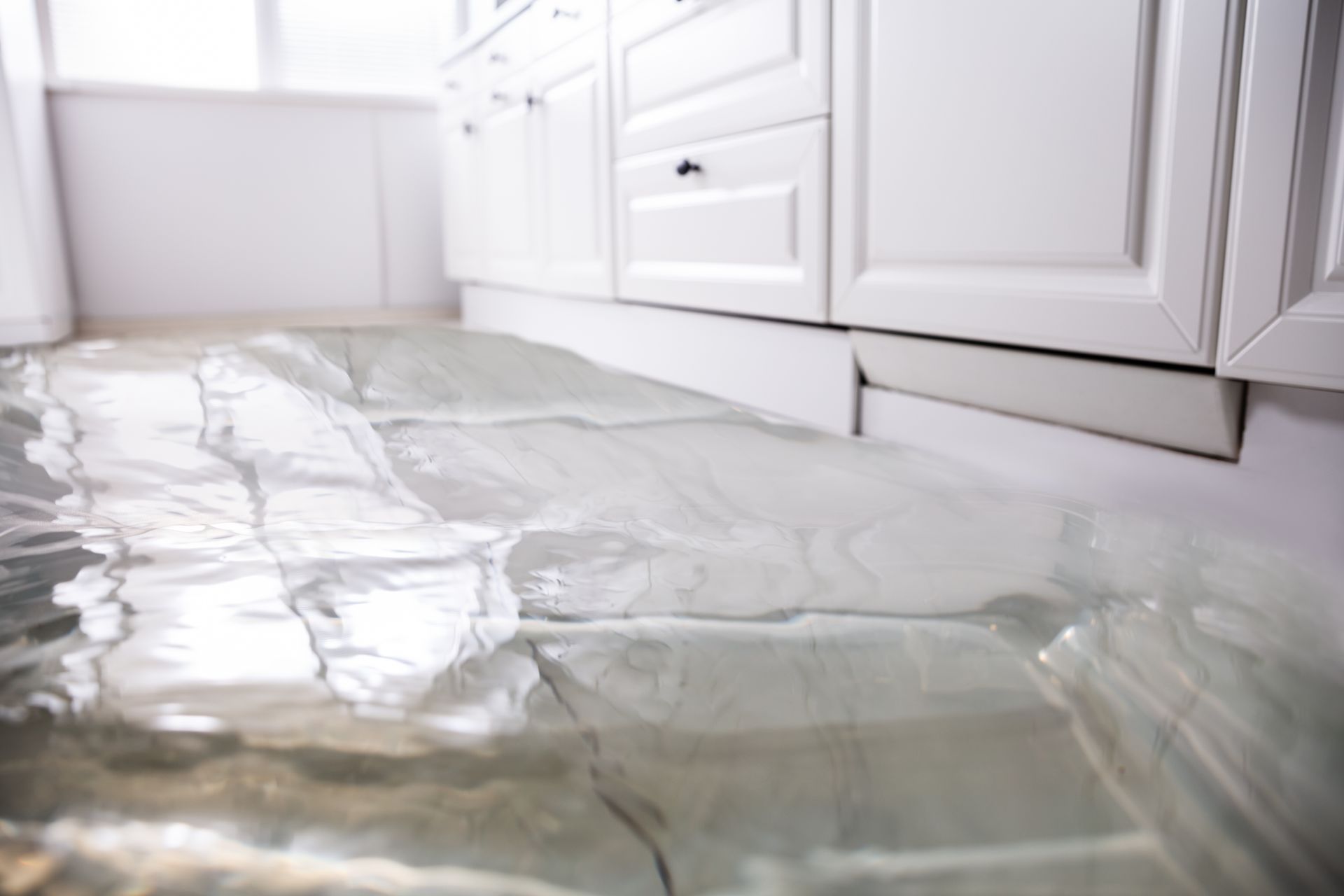 Kitchen flooded with water; white cabinets in background.